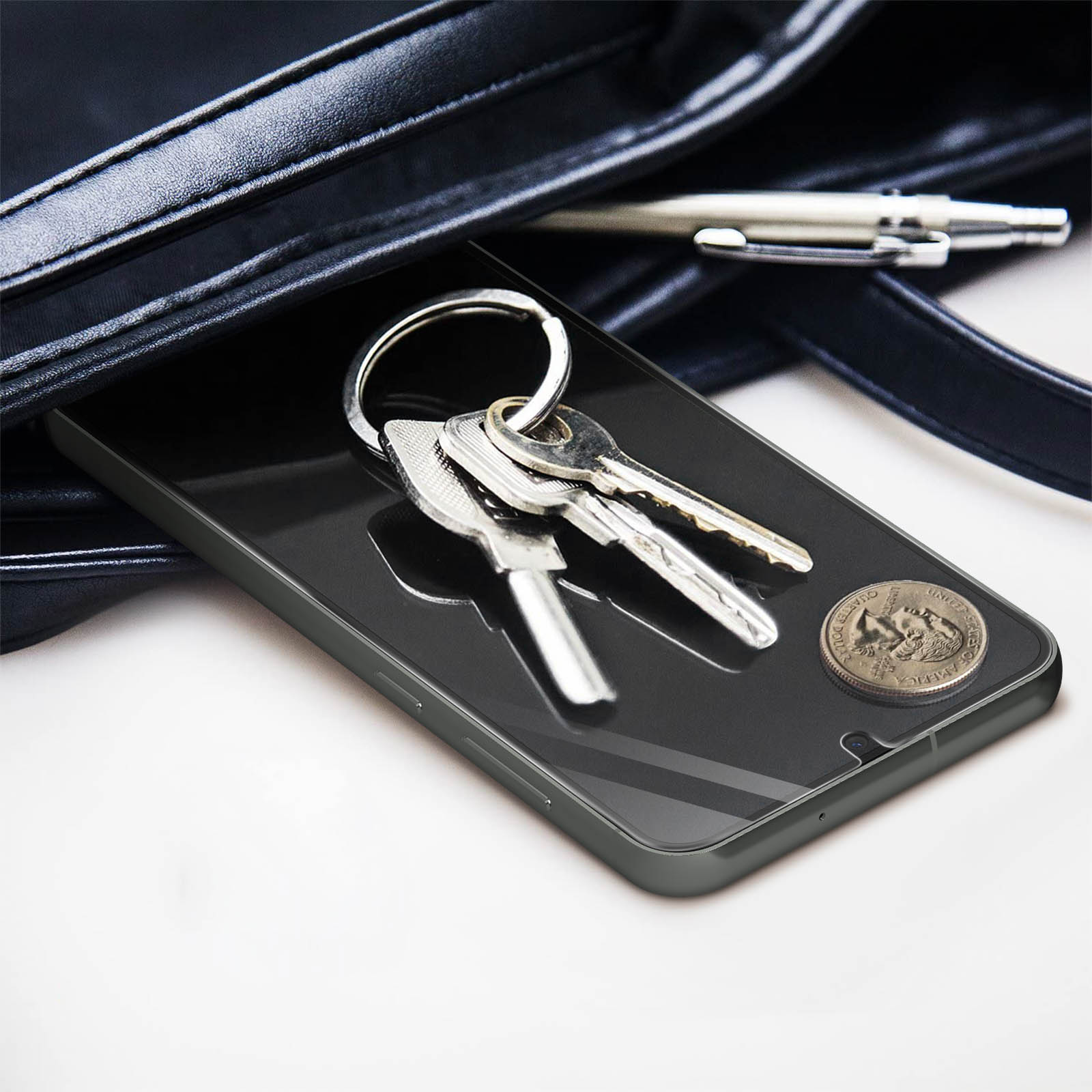 Klucze, moneta i długopis na ekranie telefonu, w czarnej torebce. Jasne tło.