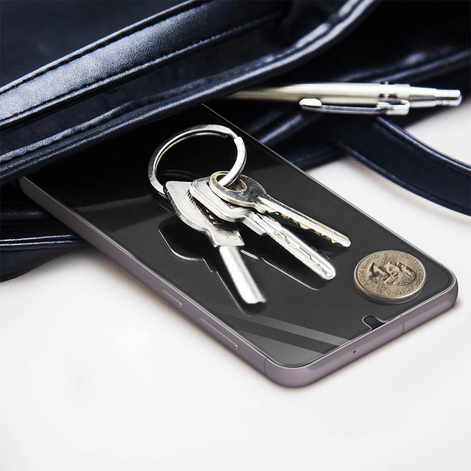 Klucze, moneta i długopis na ekranie telefonu z osłoną. Telefon jest w torbie.