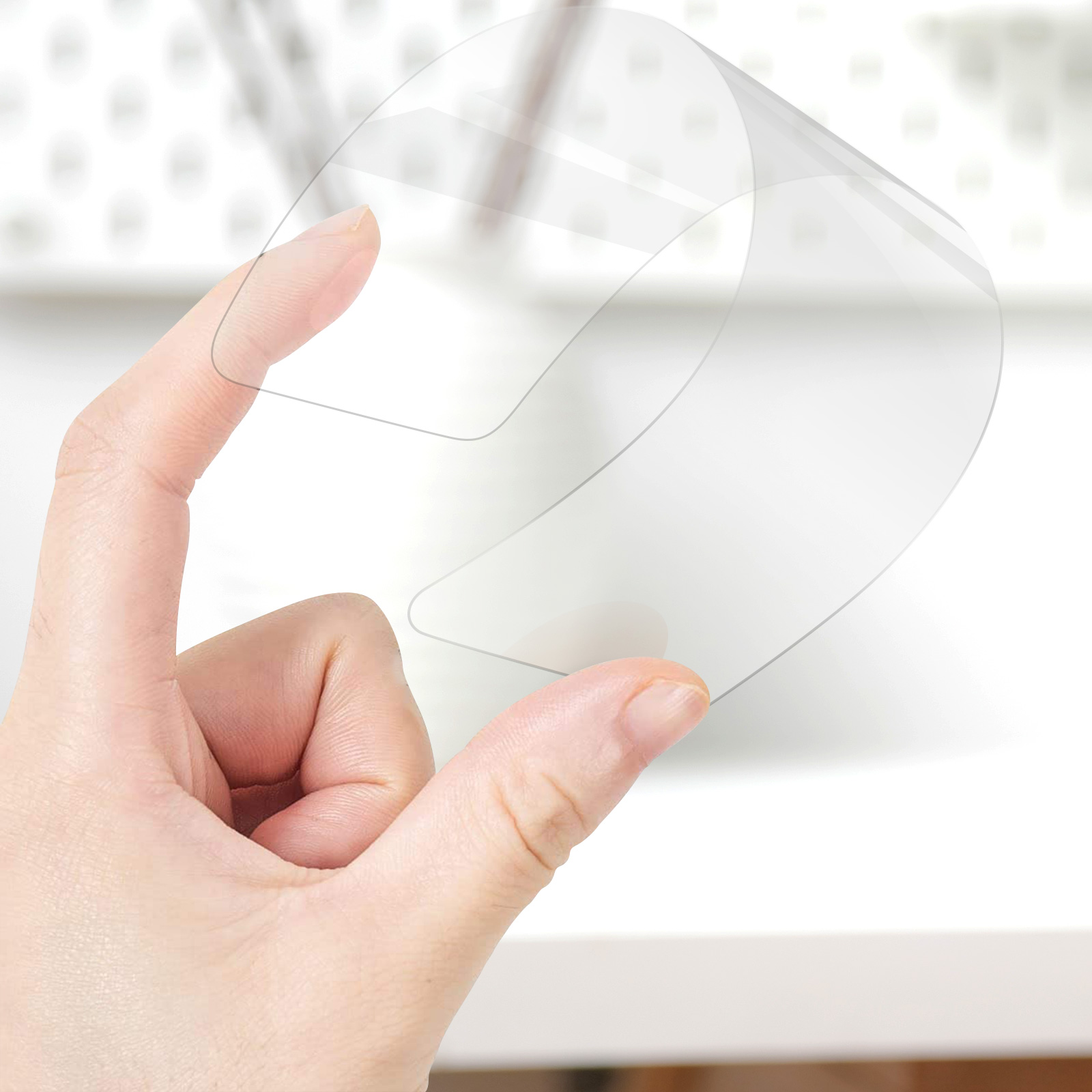 Ręka trzyma przezroczystą, elastyczną ochronę ekranu. Białe tło. Ochrona jest zakrzywiona.