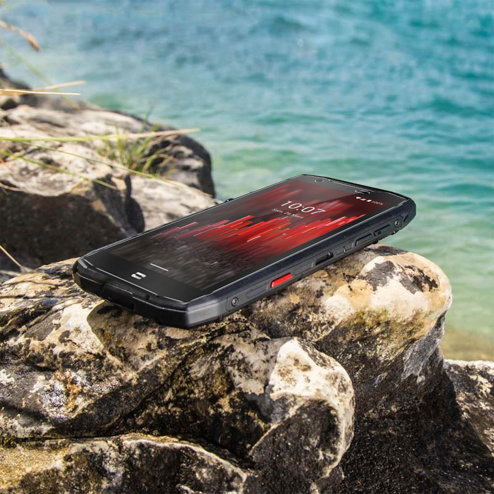 Un smartphone robuste sur un rocher près de l'océan, affichant une interface rouge.