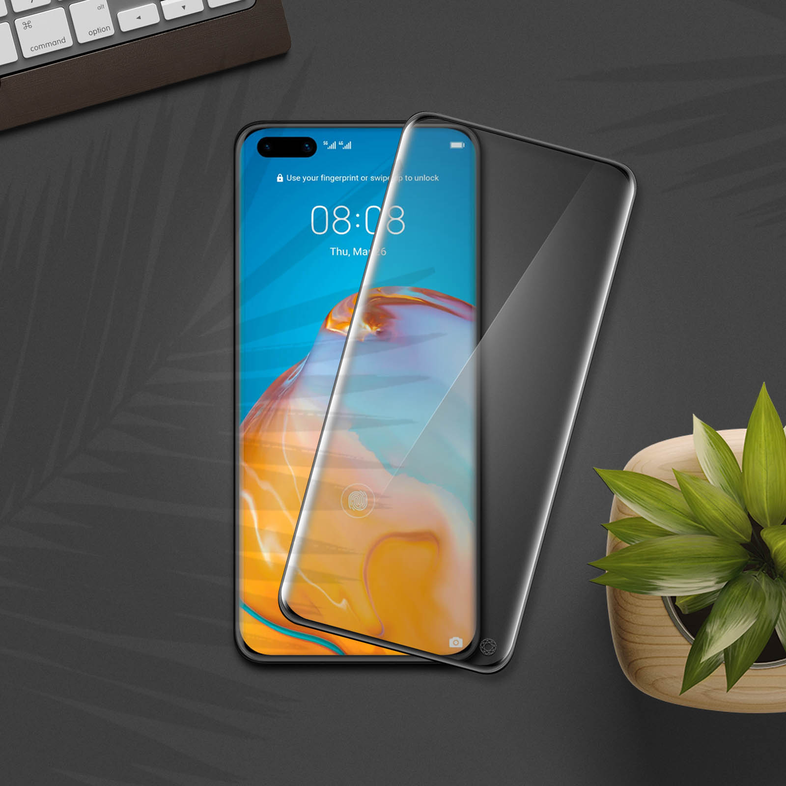 Téléphone avec protecteur d'écran installé, affichant une horloge et une notification. Un clavier et une plante à proximité.