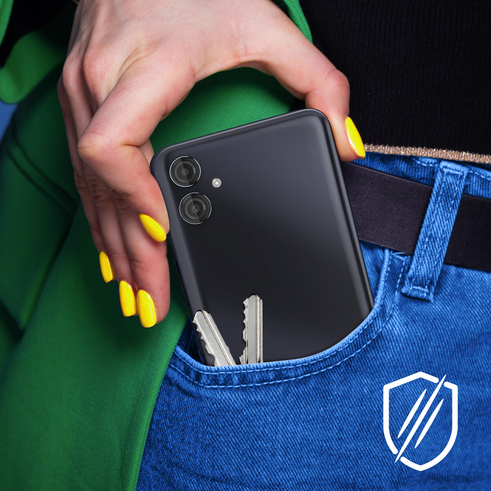 Una mano con uñas amarillas coloca un teléfono inteligente negro y llaves en un bolsillo de jeans azul. Chaqueta verde en el fondo.