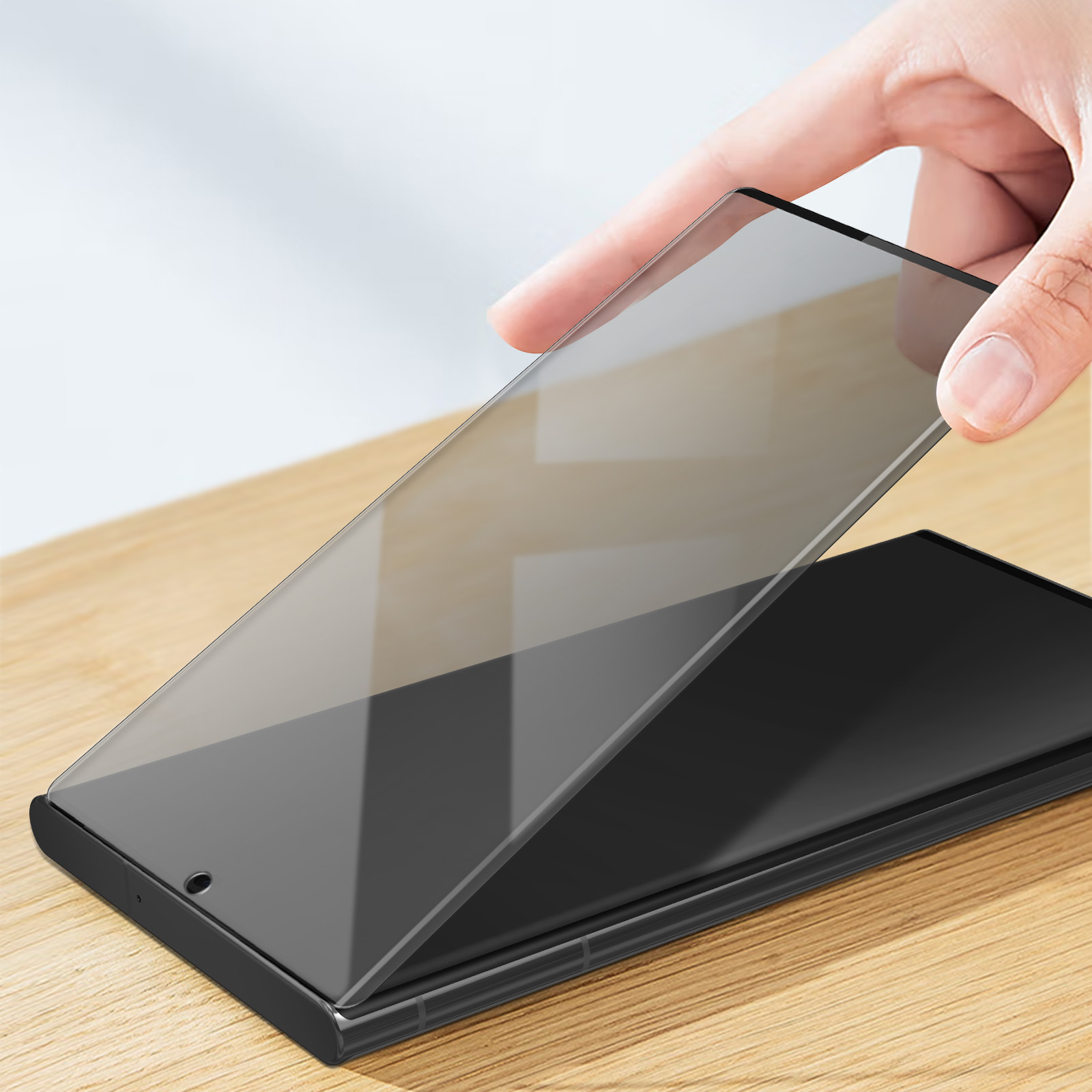 Hand die een schermbeschermer boven een telefoon houdt.