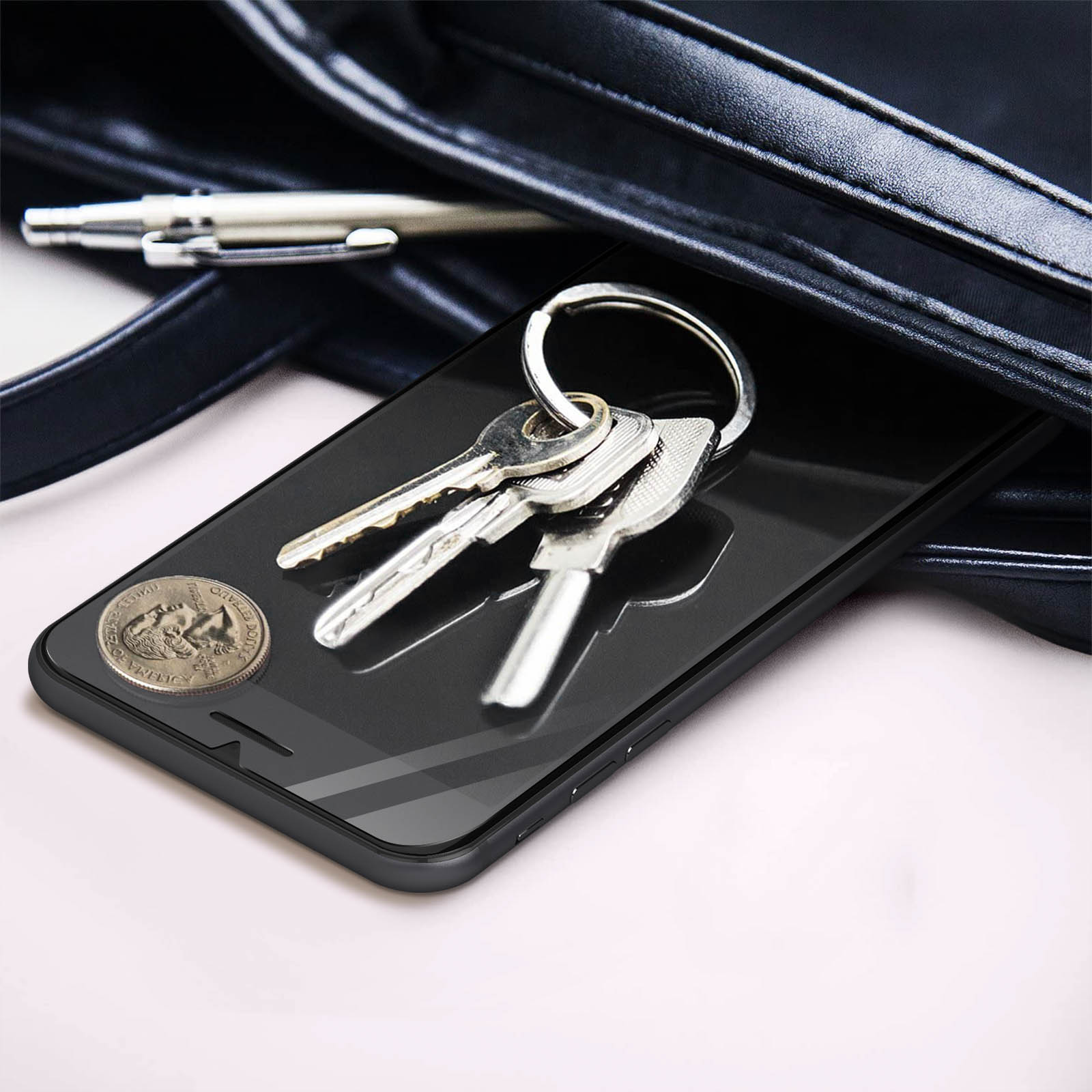 Een telefoon en sleutels in een tas. De telefoon heeft een zwart scherm en de tas is zwart. Een munt ligt naast de sleutels.