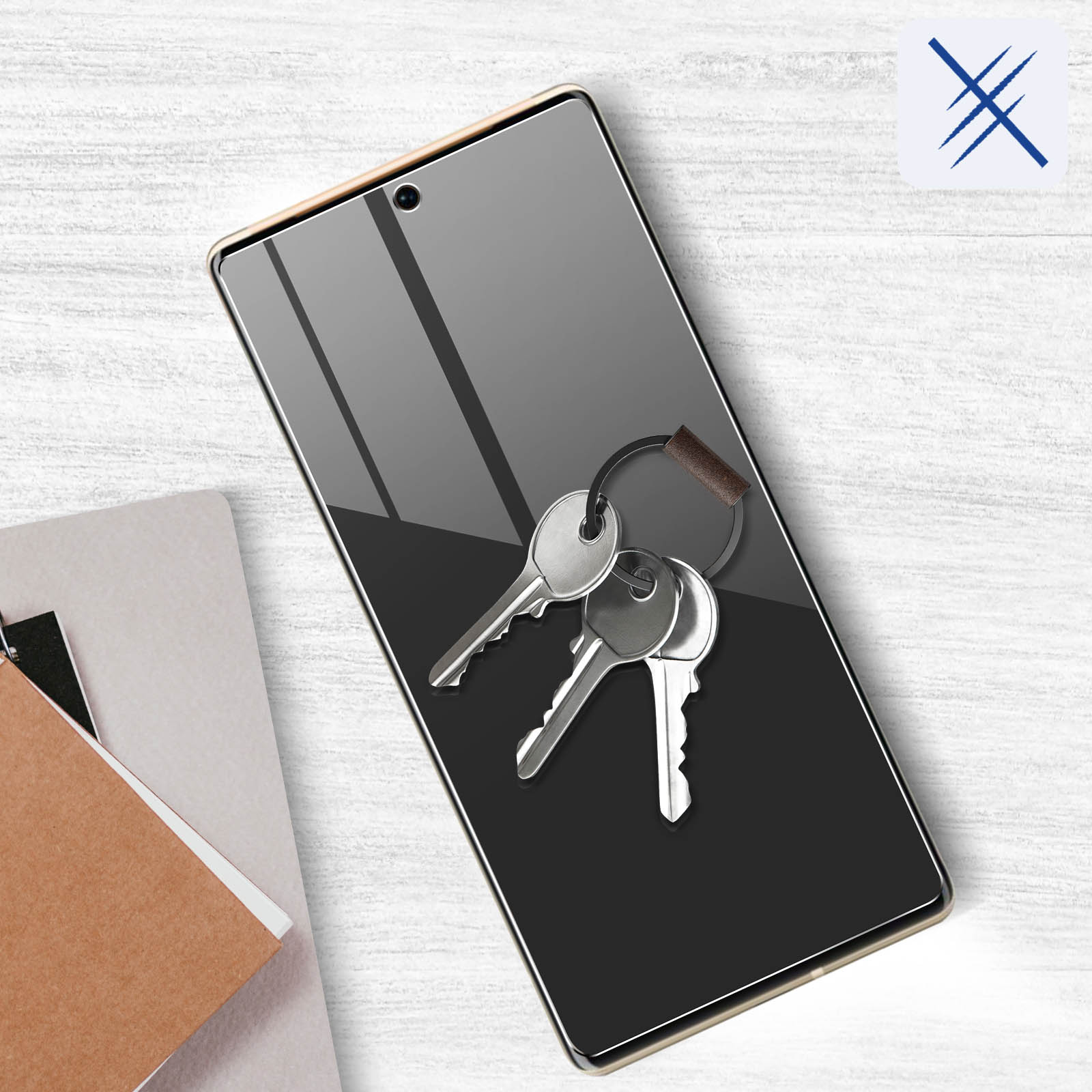 Telefon z kluczami. Telefon ma ochraniacz ekranu. Z lewej strony znajduje się notatnik.