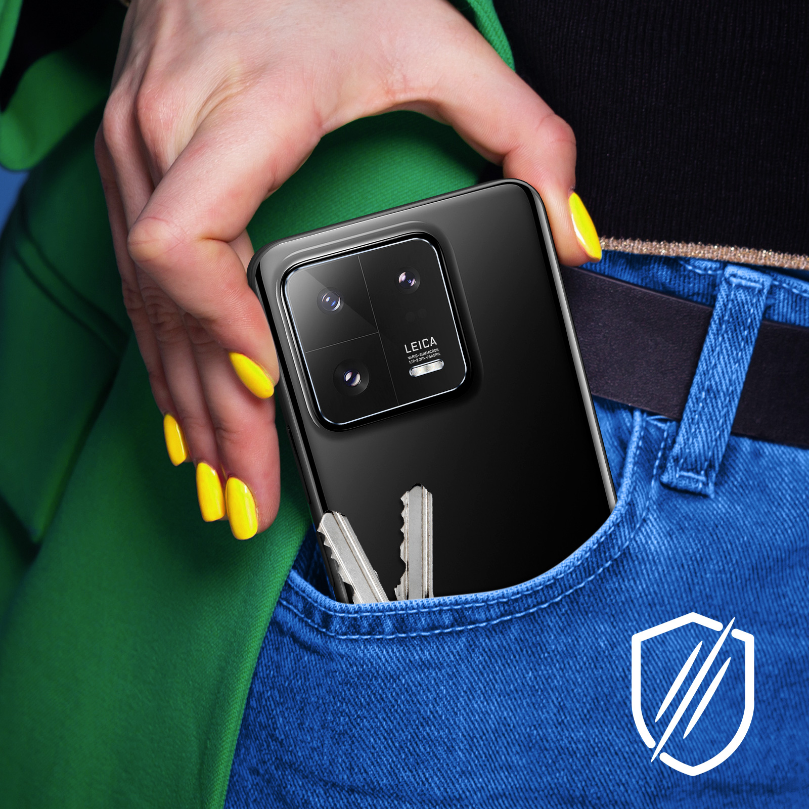 Dłoń trzymająca czarny telefon z modułem kamery. Telefon jest w kieszeni jeansów. Klucze są w kieszeni.