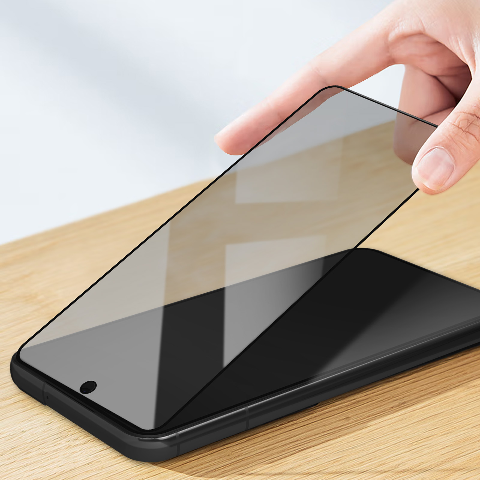Hand plaatst screenprotector op zwarte smartphone op houten tafel.