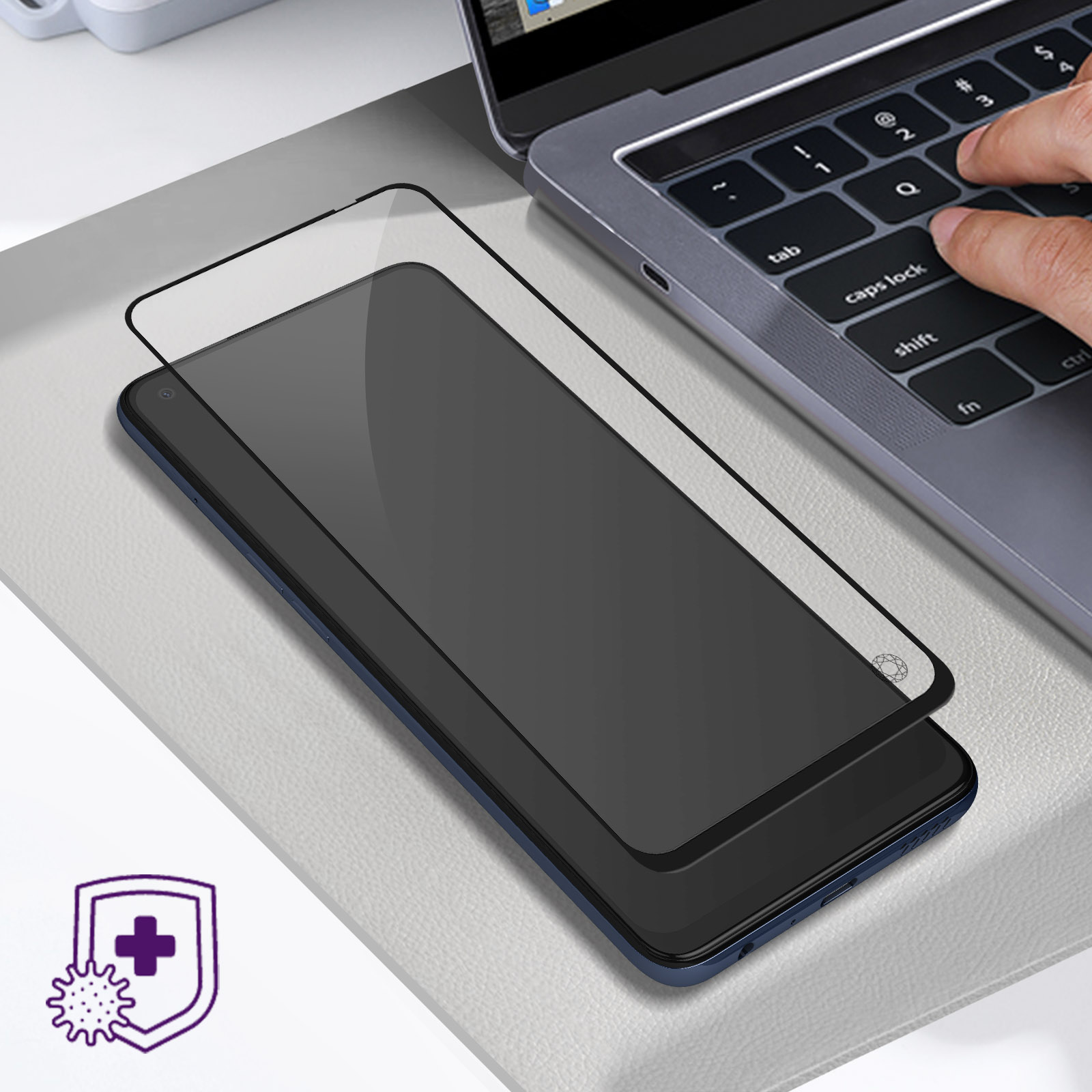 Telefono con protezione schermo su una superficie grigia, accanto alla tastiera di un laptop. Una mano digita.