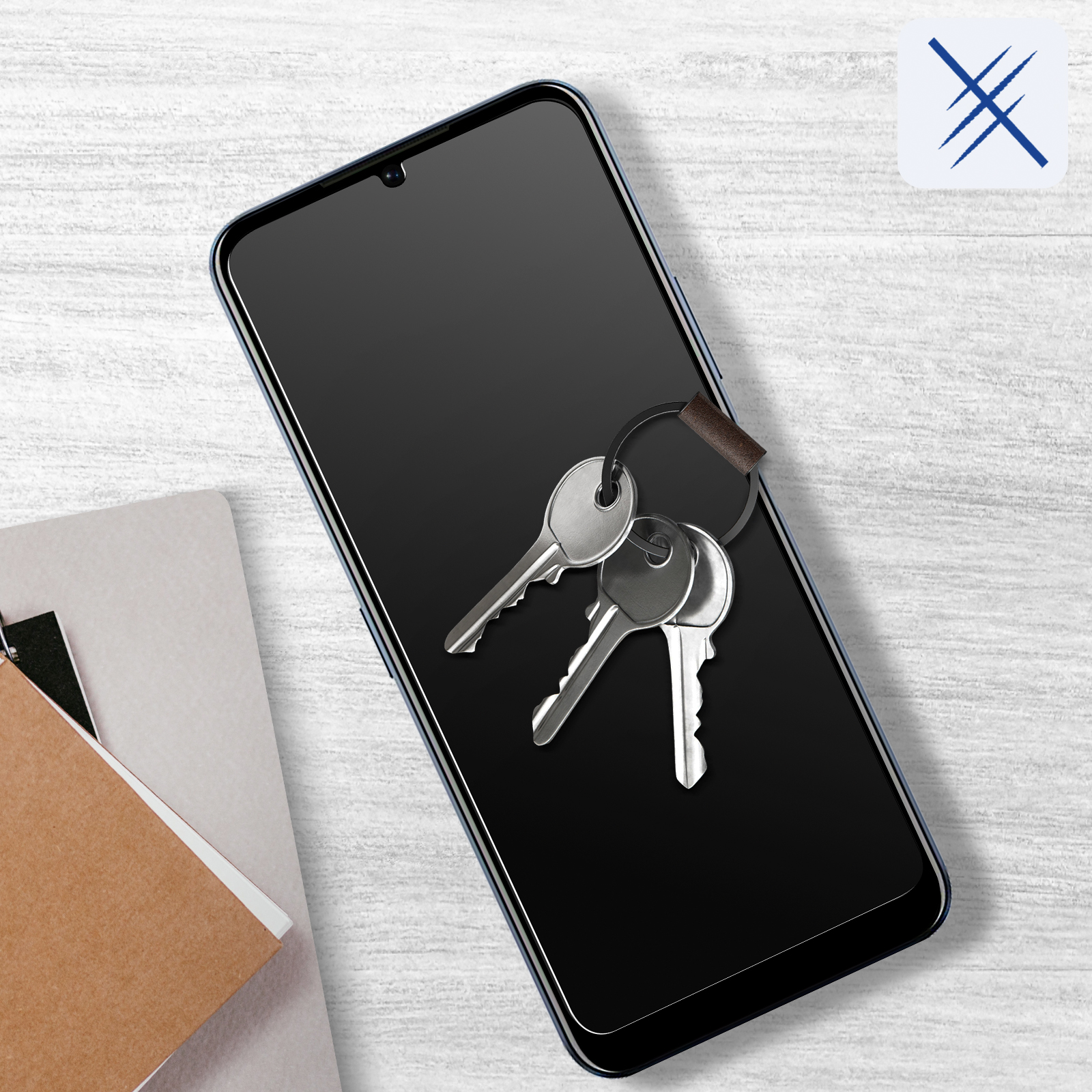 Telefon z kluczami. Telefon ma ochraniacz ekranu. Z lewej strony znajduje się notatnik.