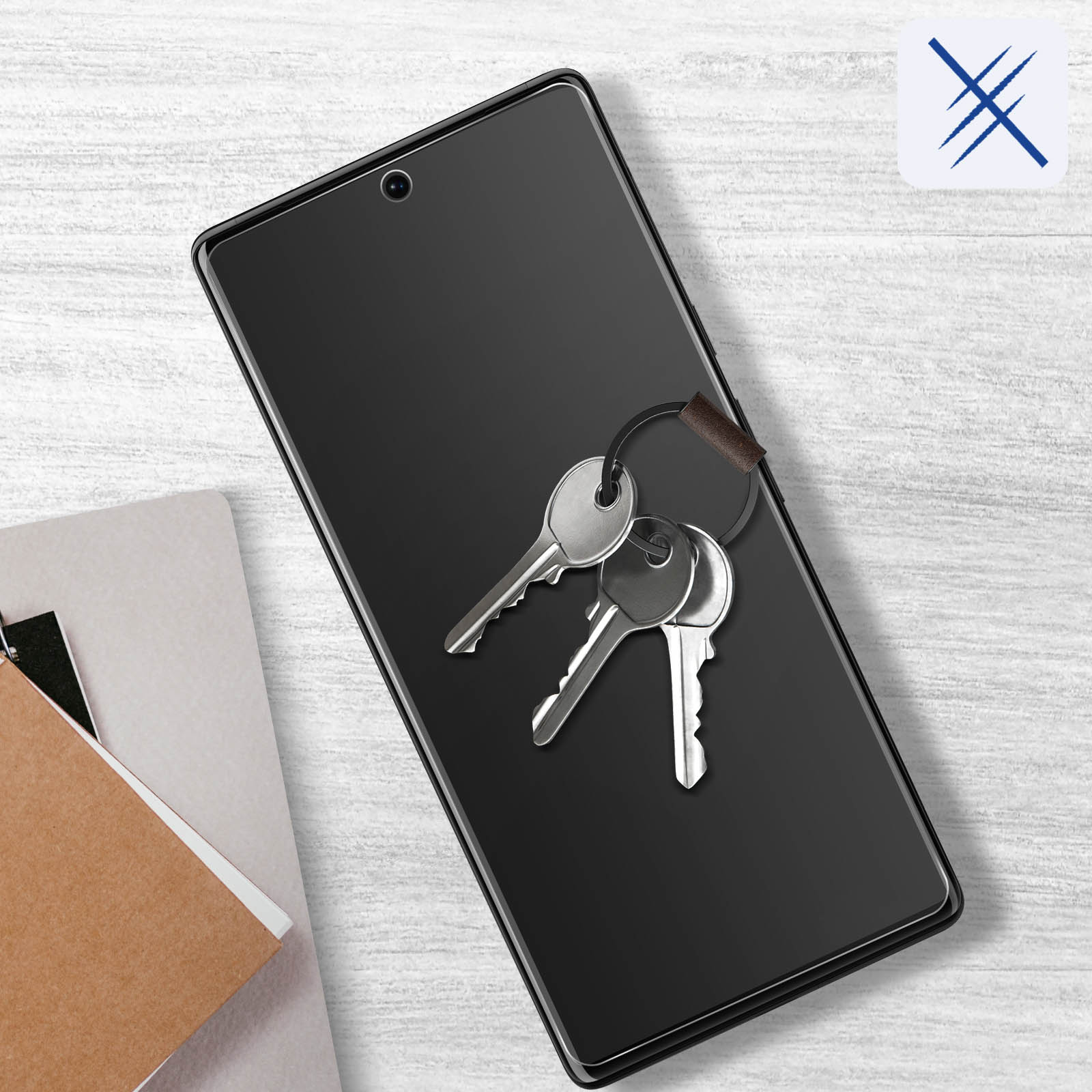 Klucze na telefonie z osłoną ekranu. Telefon leży na drewnianej powierzchni w pobliżu notatników.