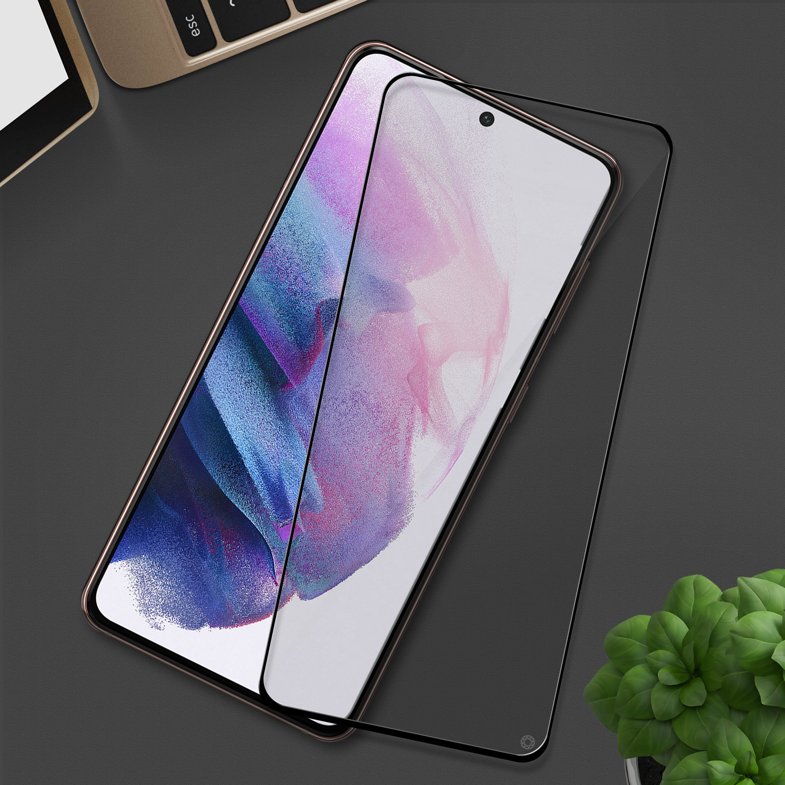 Un smartphone avec un protecteur d'écran sur une surface sombre, avec un clavier et une plante en arrière-plan.