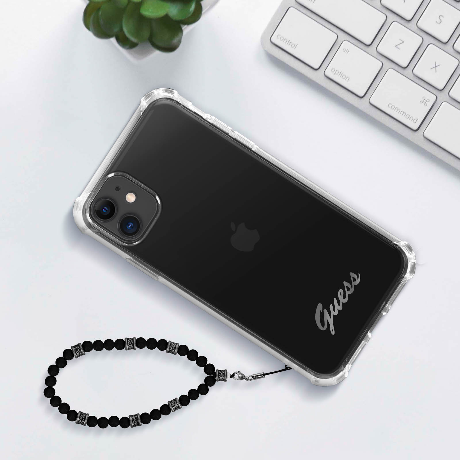 Telefon in klarer Guess-Hülle mit Perlenarmband und Tastatur im Hintergrund.