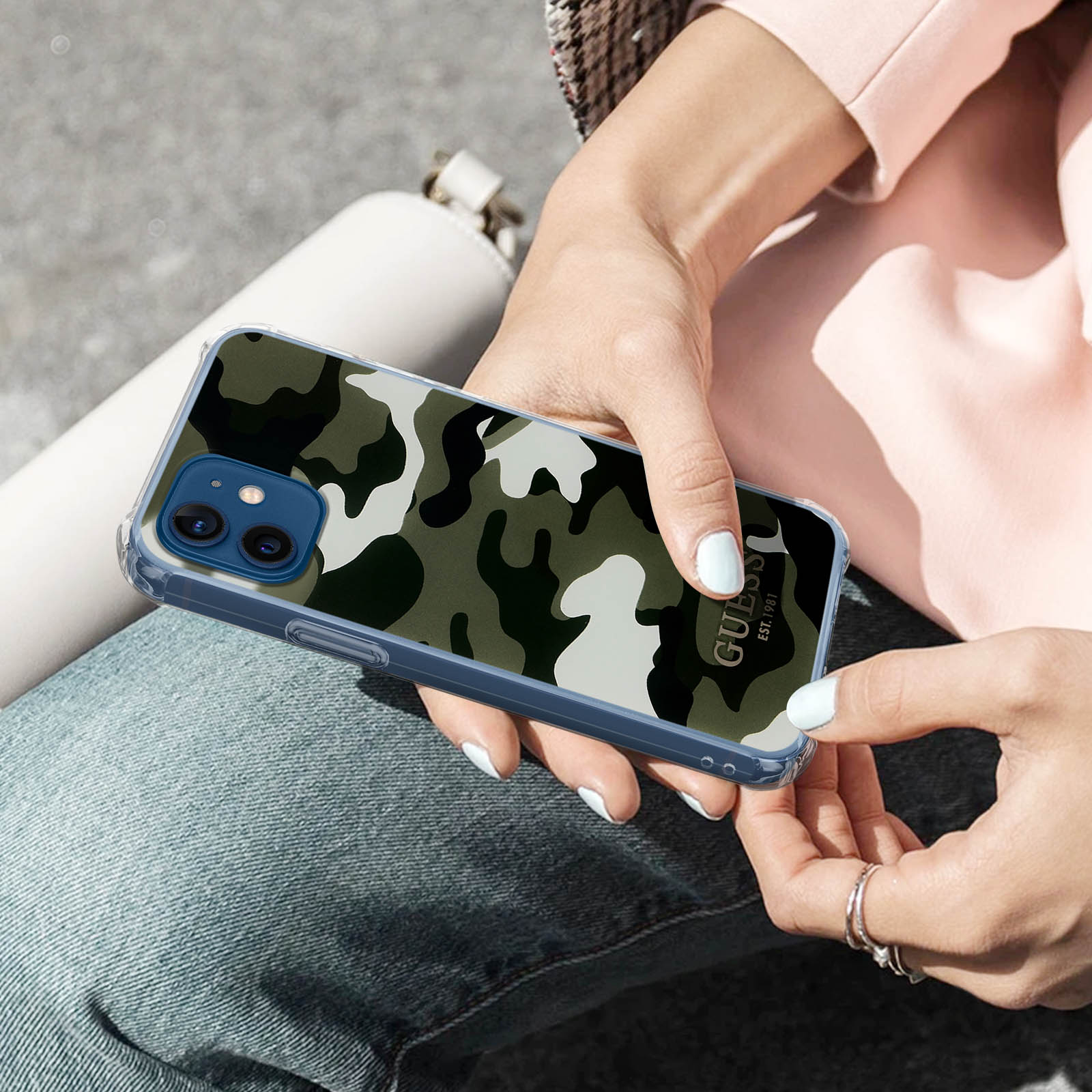 Donna che tiene un telefono in una custodia mimetica. Indossa un top rosa e jeans.