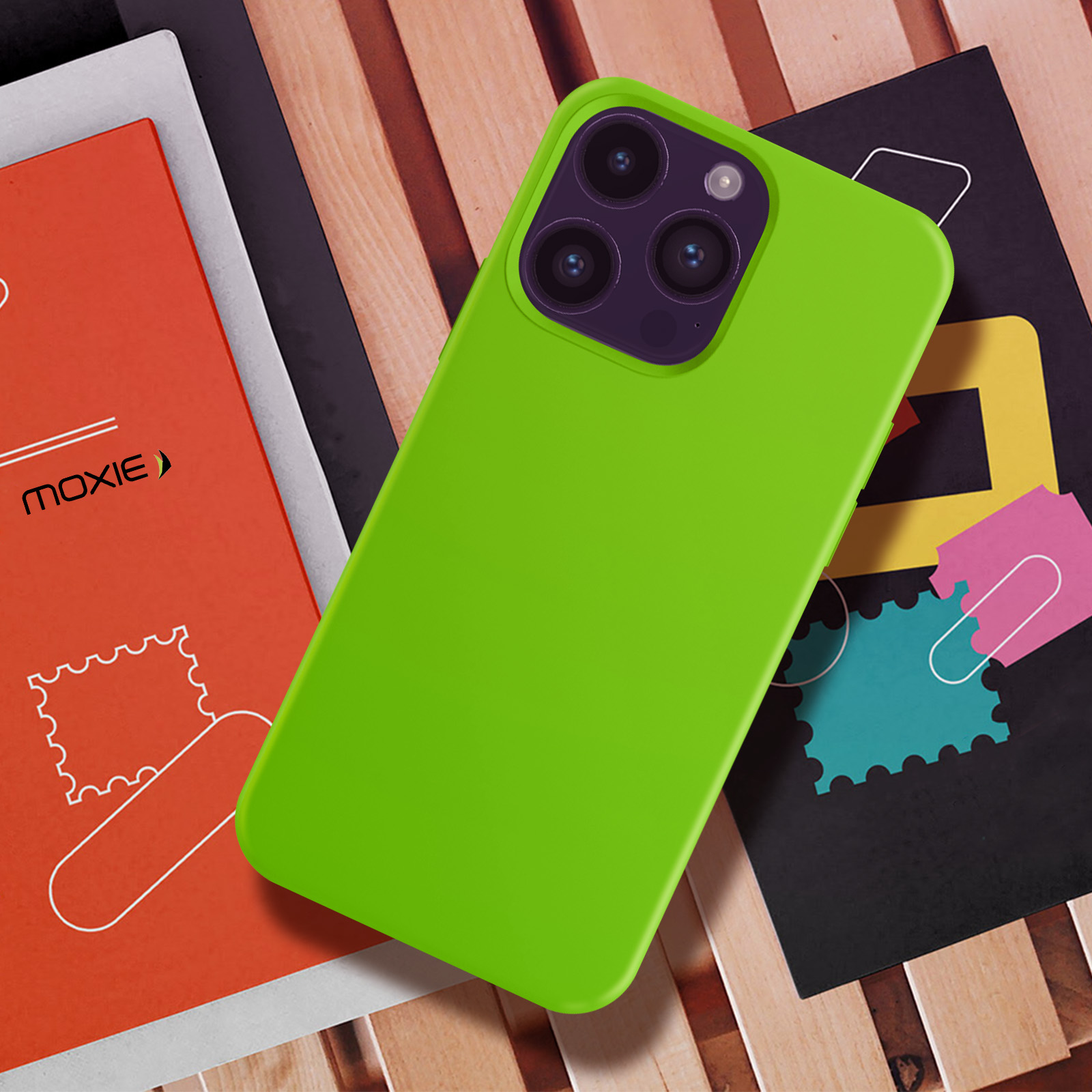 Coque de téléphone verte sur une surface en bois, avec des livres et des images de type timbre en arrière-plan.