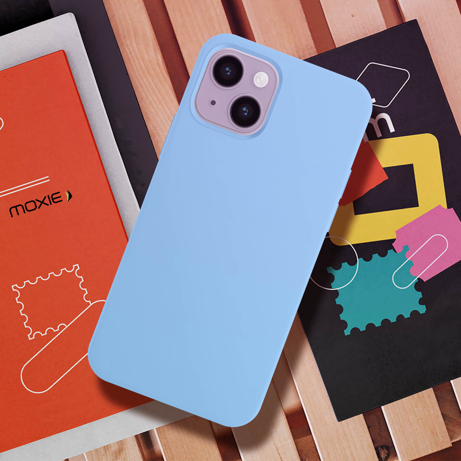 Une coque de téléphone bleue sur une table en bois avec des livres et un magazine. La coque est de couleur bleu clair.