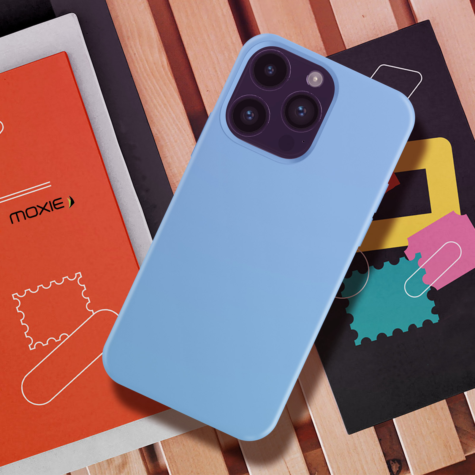 Een blauwe telefoonhoes op een houten oppervlak, met boeken en een tijdschrift. Telefoon heeft meerdere camera's.