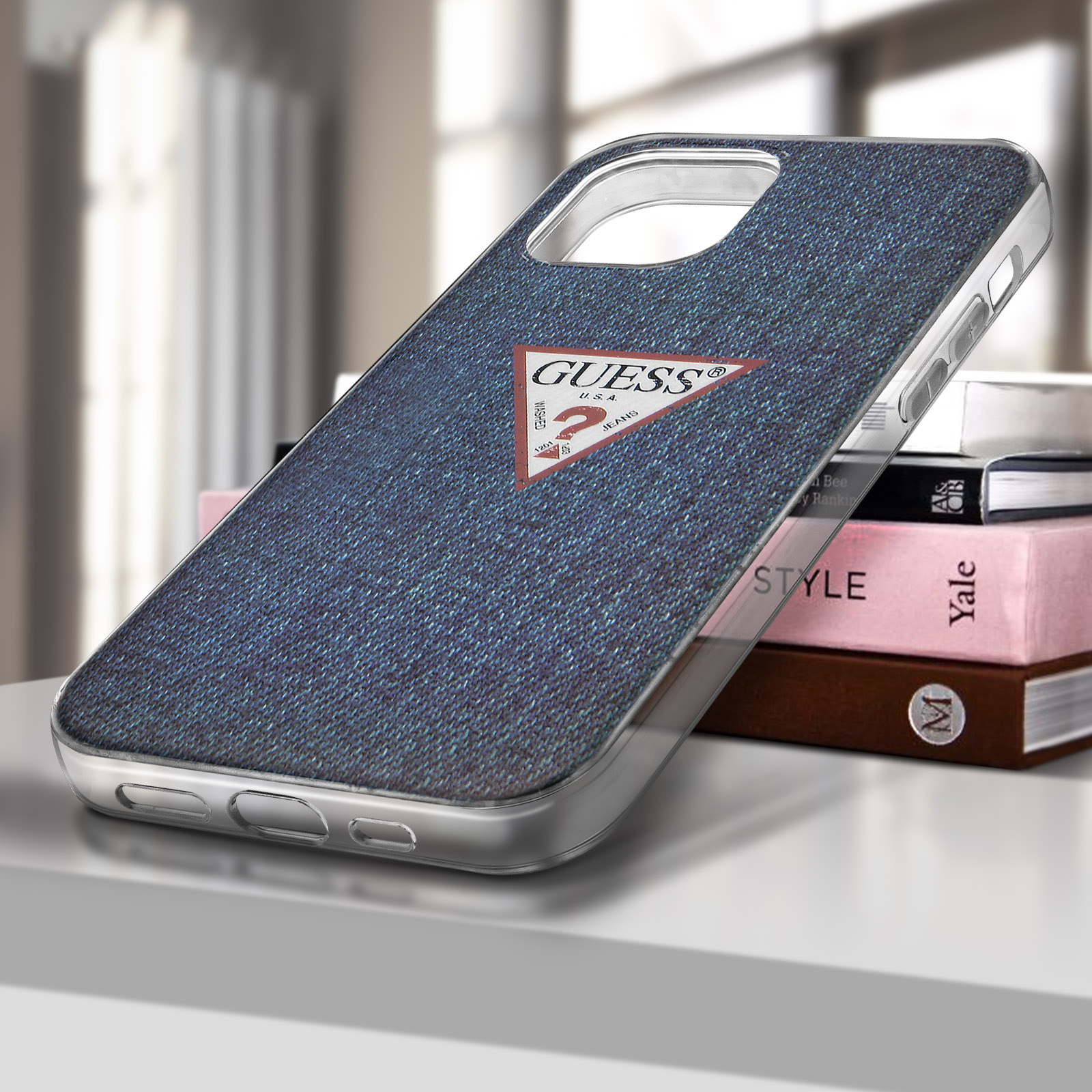 Etui na telefon z dżinsu na stole z książkami. Etui ma logo Guess.