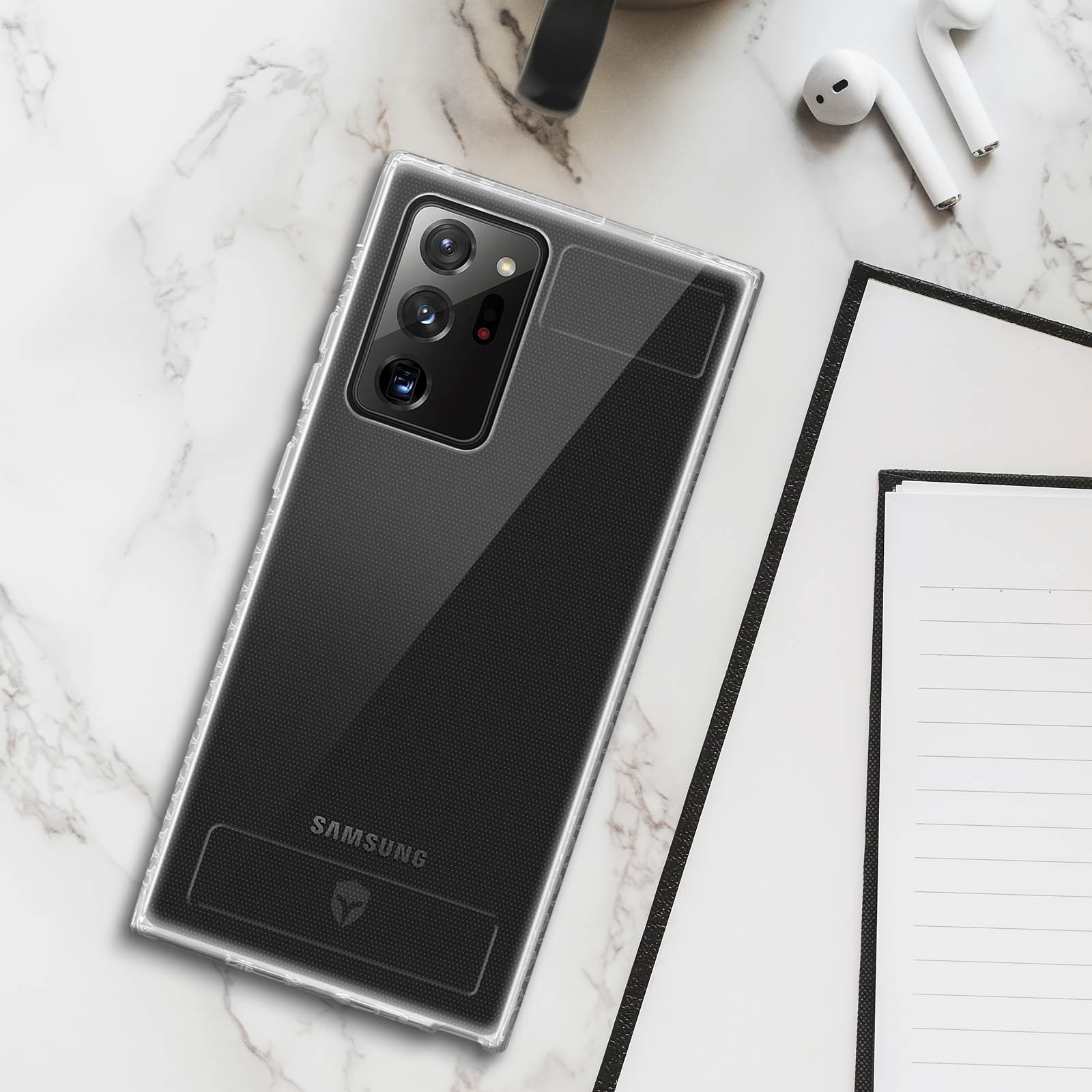 Téléphone dans un étui transparent sur marbre, avec écouteurs et carnet en arrière-plan.