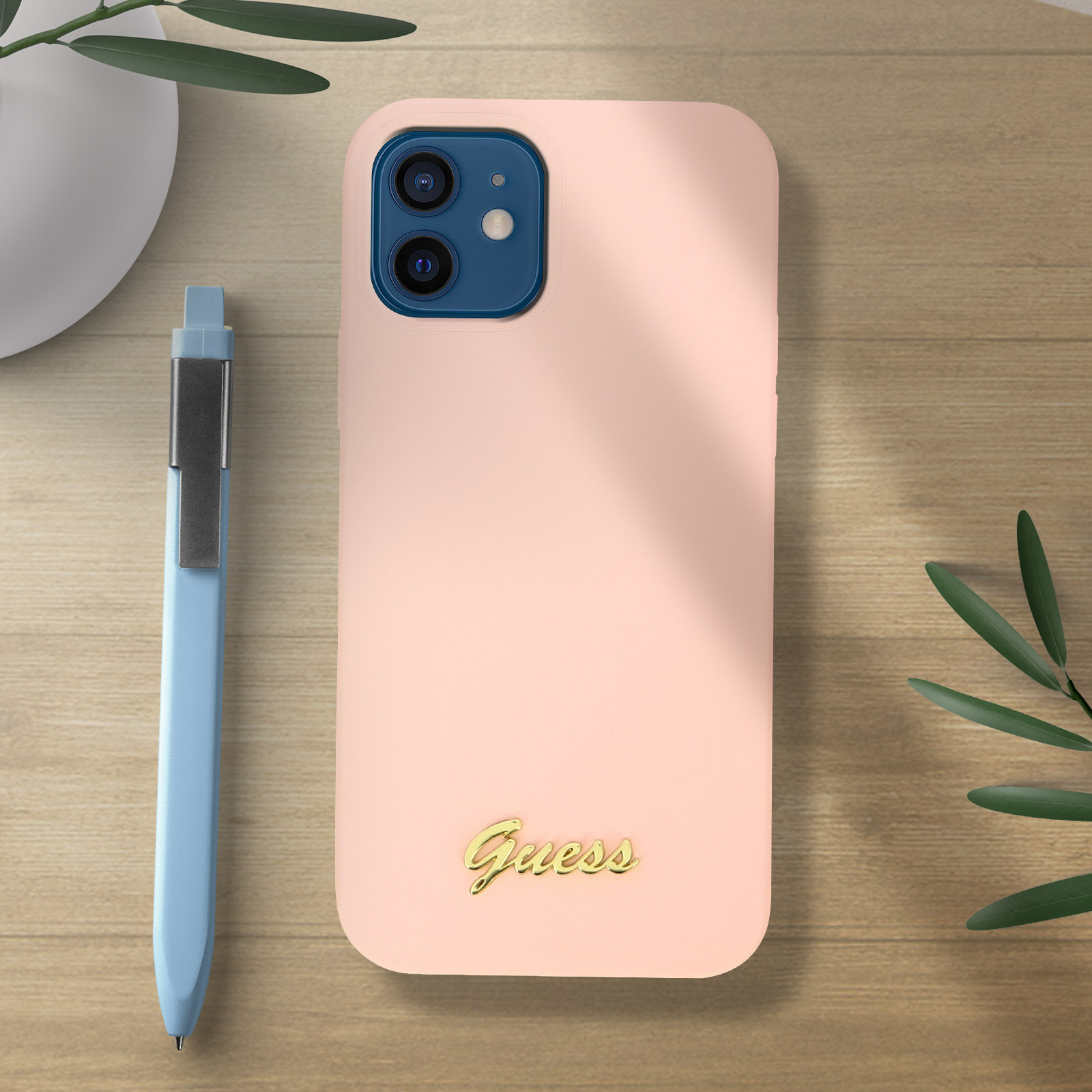 Eine rosa Handyhülle mit dem Wort Guess und einem blauen Stift auf einem Holztisch.