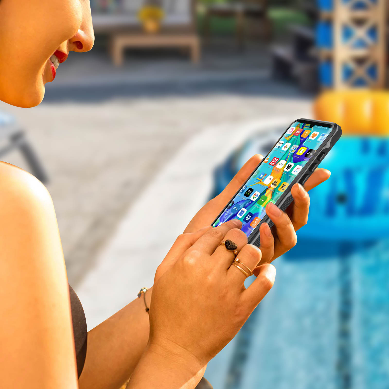 Donna che tiene un telefono con schermo pieno di app. È vicino a una piscina.