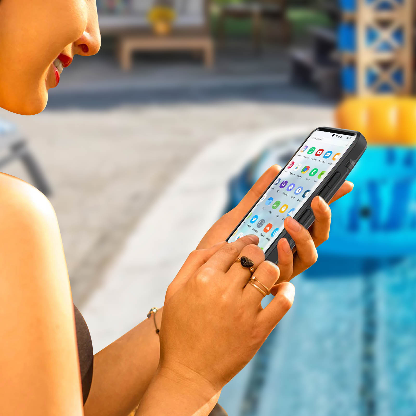 Donna che tiene un telefono con app aperte vicino a una piscina. Sta sorridendo.