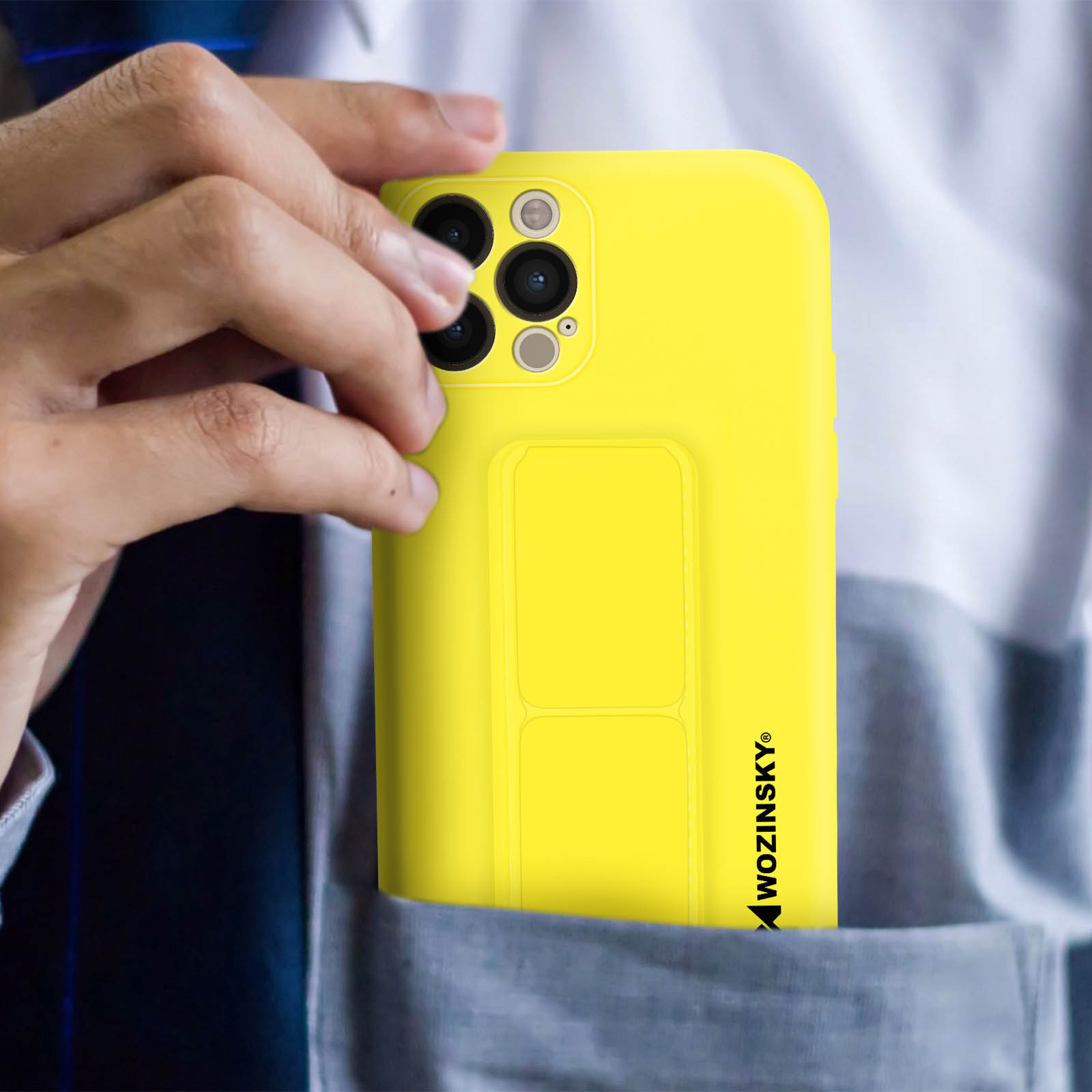 Ręka trzymająca żółty telefon w kieszeni, pokazująca aparat i podpórkę.