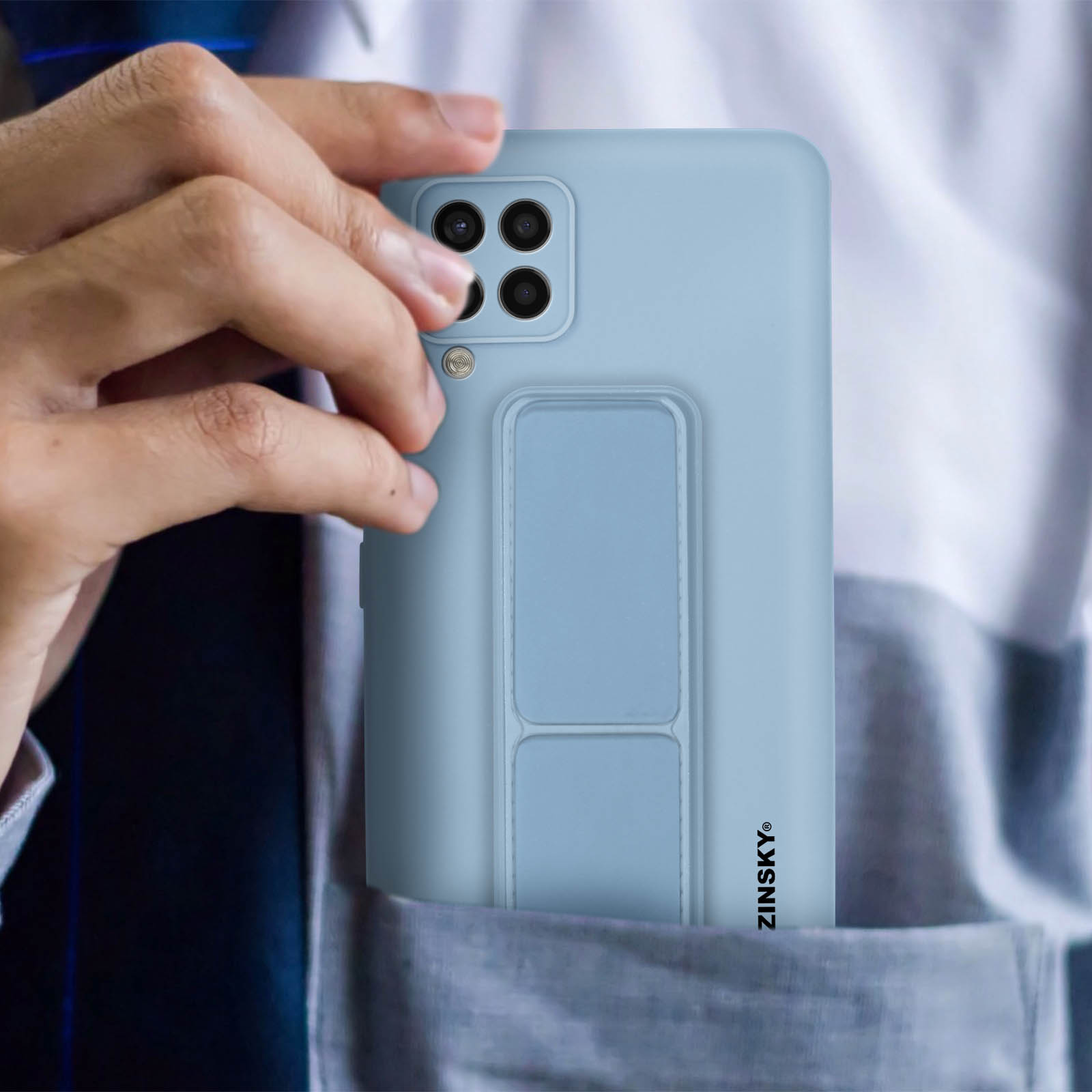 Dłoń trzymająca jasnoniebieski telefon ze stojakiem. Telefon jest w kieszeni.