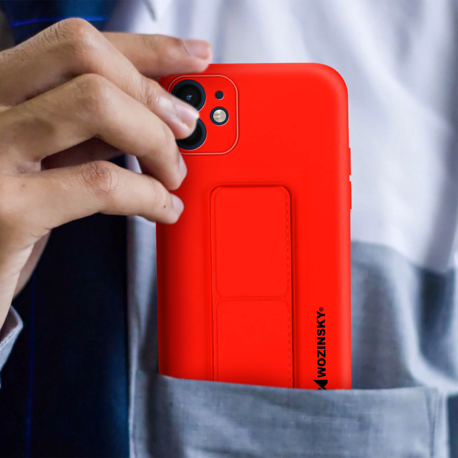 Dłoń trzymająca czerwony telefon w kieszeni. Telefon ma podpórkę.