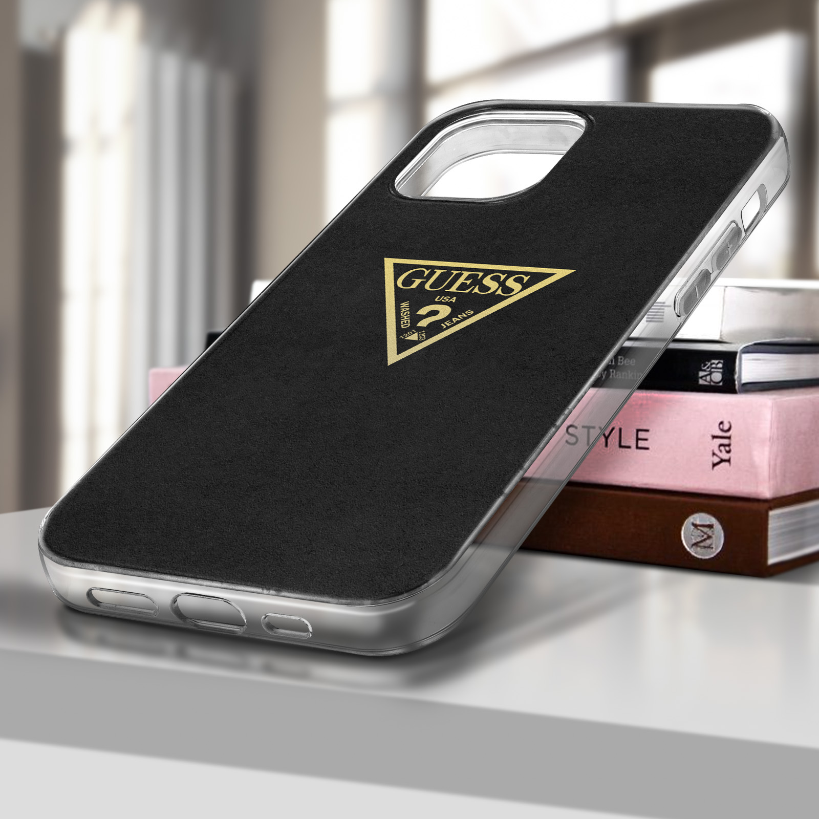 Custodia per telefono con logo GUESS su sfondo nero e bordo trasparente. Libri sul tavolo.