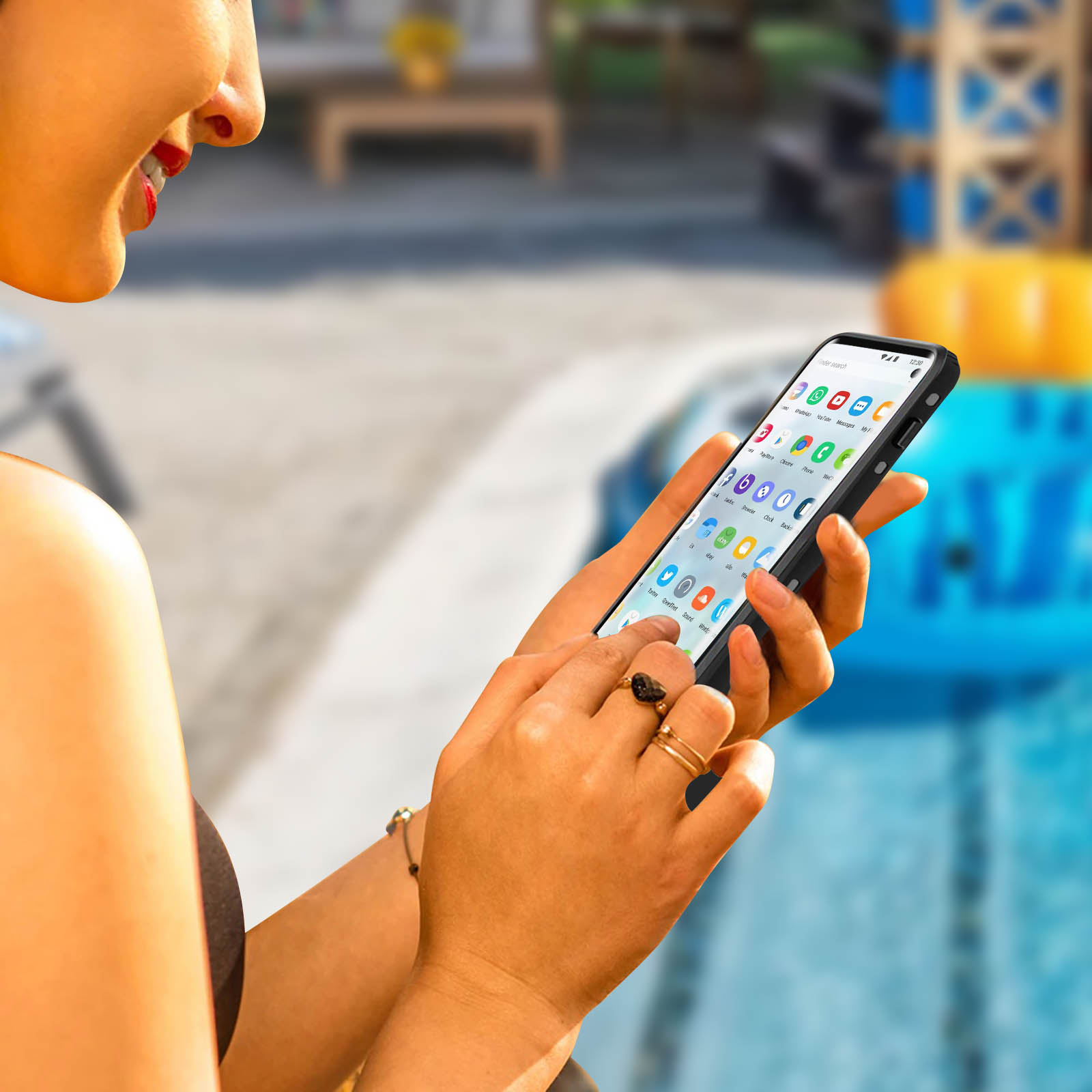 Donna che tiene il telefono, sorridente. Il telefono mostra app. Piscina sfocata sullo sfondo.