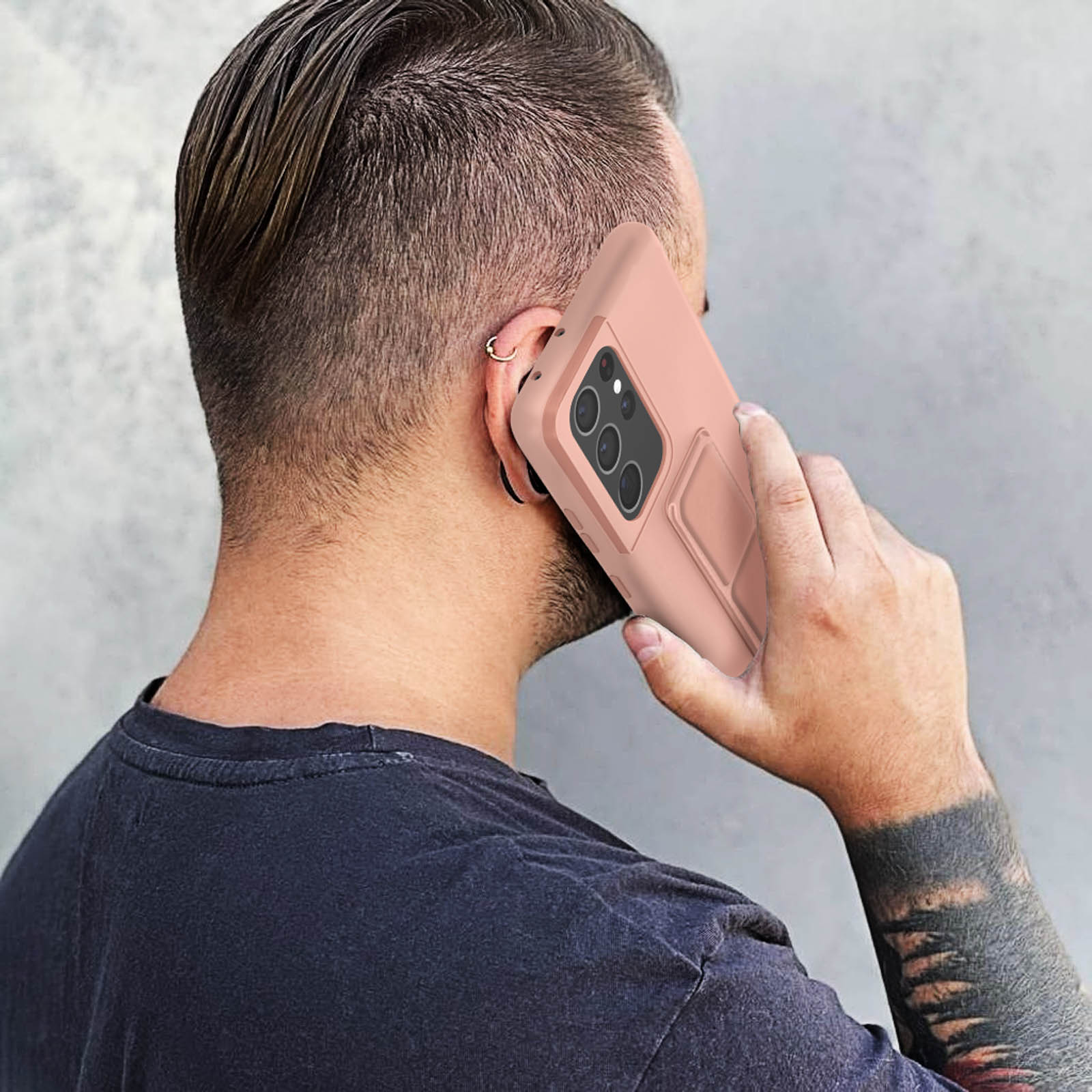 Mężczyzna trzyma różowy telefon przy uchu. Telefon ma etui z podstawką. Jest odwrócony tyłem.