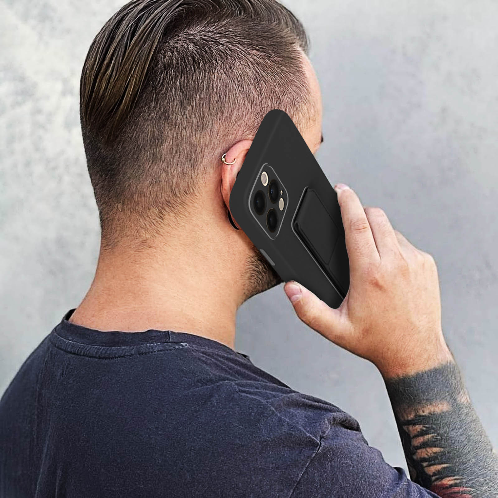 Mężczyzna trzyma czarny telefon z otwartą podpórką. Telefon przy uchu.