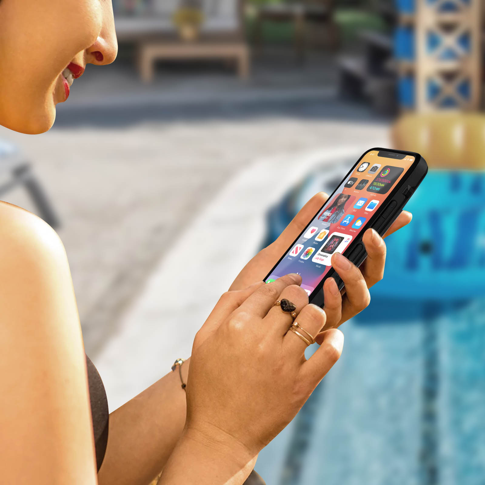 Una donna tiene in mano un telefono con una custodia vicino a una piscina, mostrando un'interfaccia dell'app sullo schermo.
