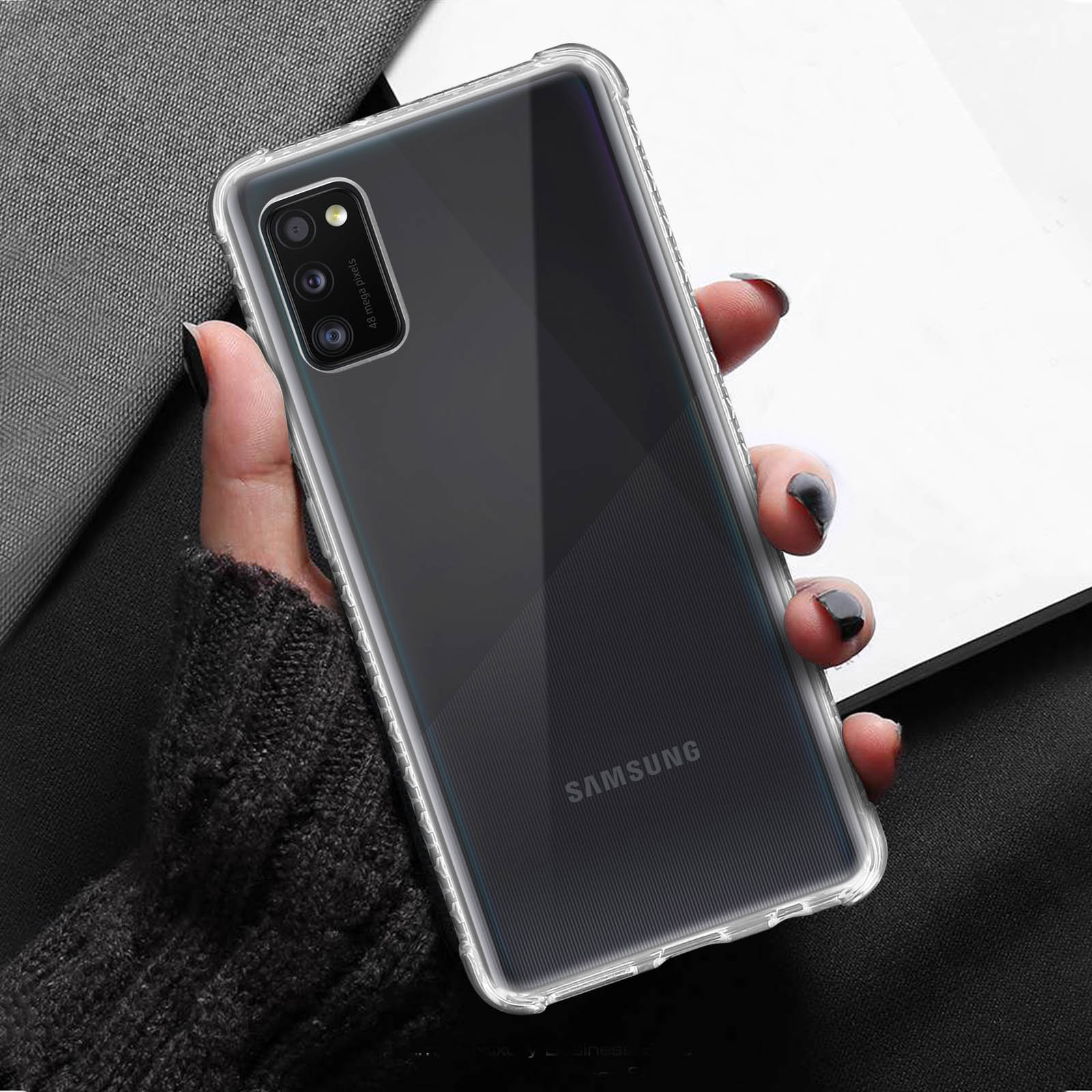 Une main tenant une coque de téléphone transparente sur un fond noir avec une feuille de papier blanche.