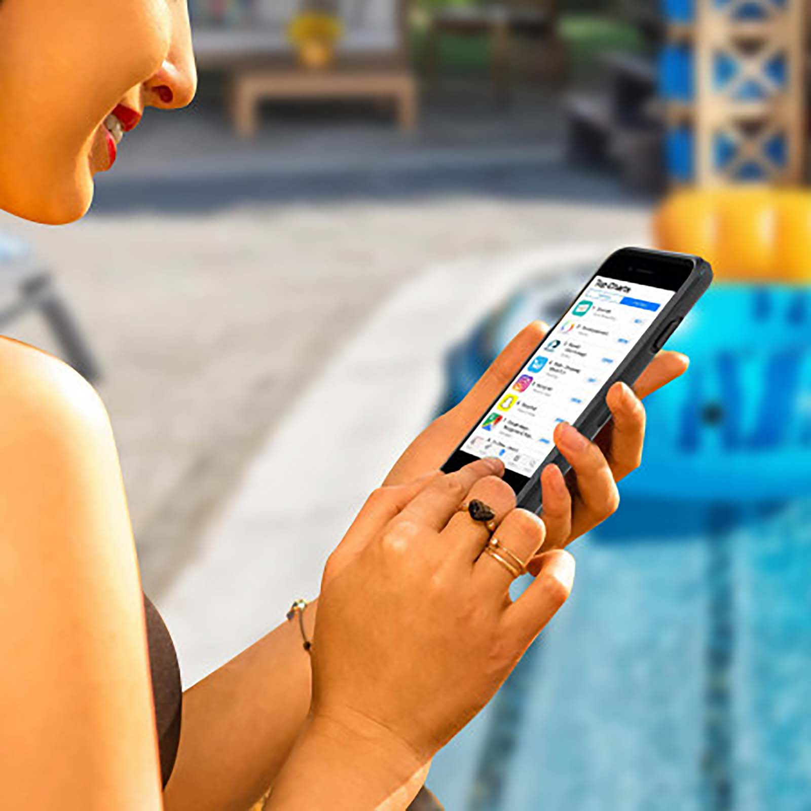 Frau benutzt Telefon am Pool, App-Bildschirm sichtbar.