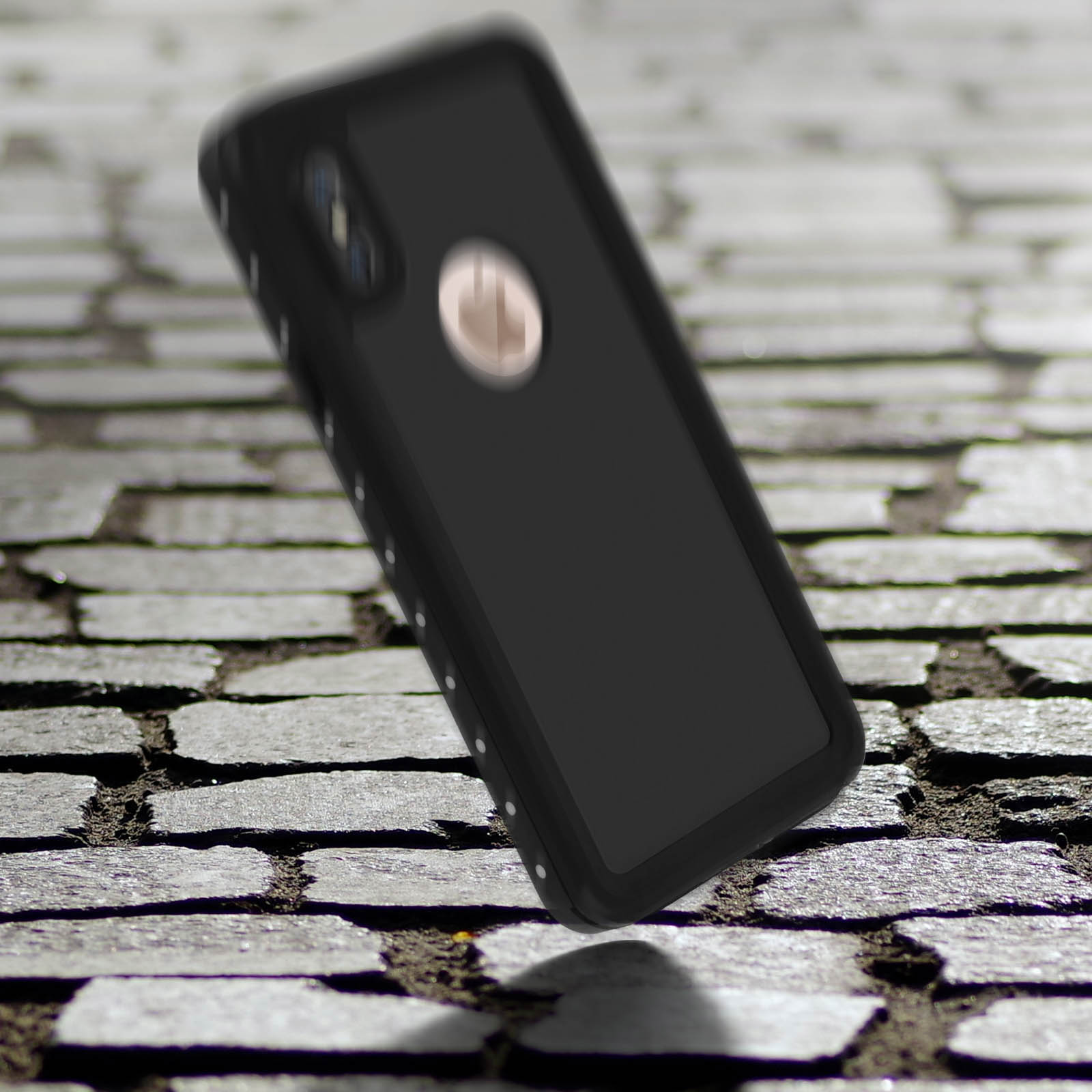 Una custodia nera per telefono sta cadendo. Ha una doppia fotocamera e un anello color oro. Lo sfondo è pietra.
