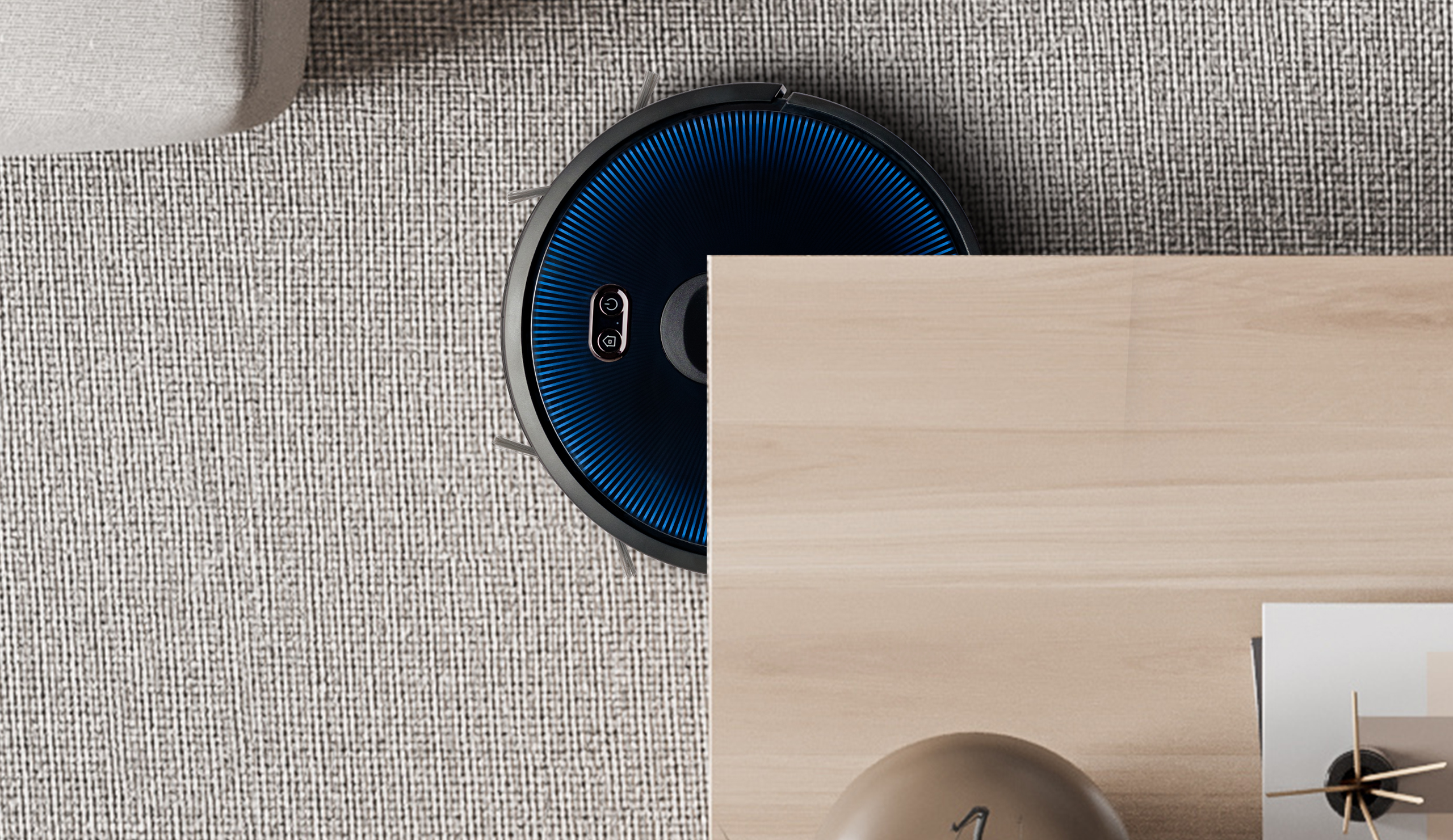 Odkurzacz automatyczny na dywanie obok drewnianego stołu. Odkurzacz jest czarny i niebieski.