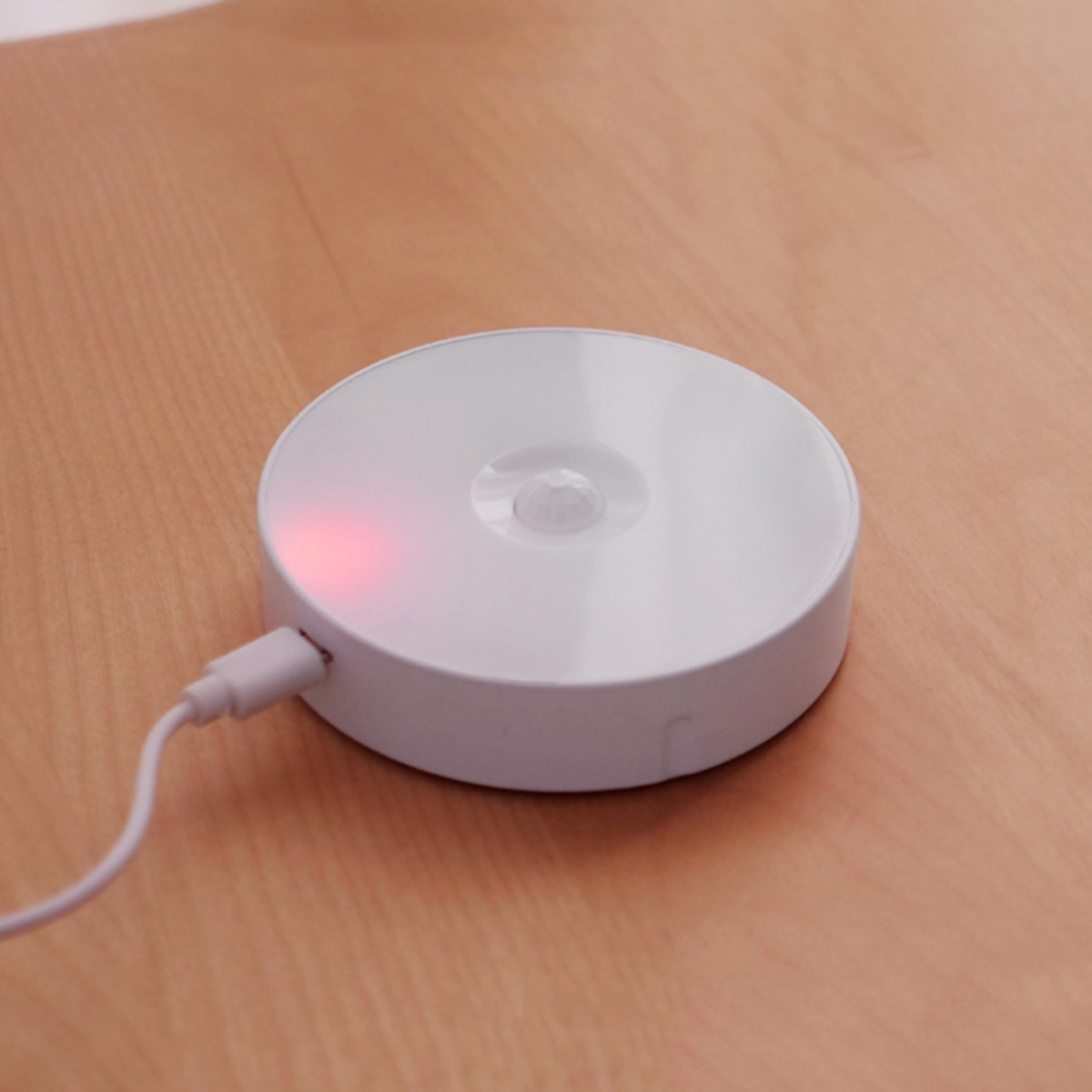 Un dispositivo blanco y redondo con un cable blanco enchufado sobre una superficie de madera.