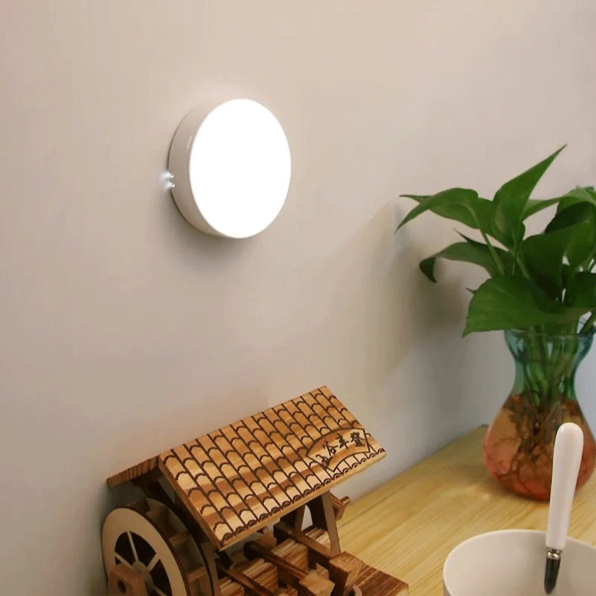 Una luz LED redonda blanca en una pared, con una rueda de agua de madera y plantas a la vista.