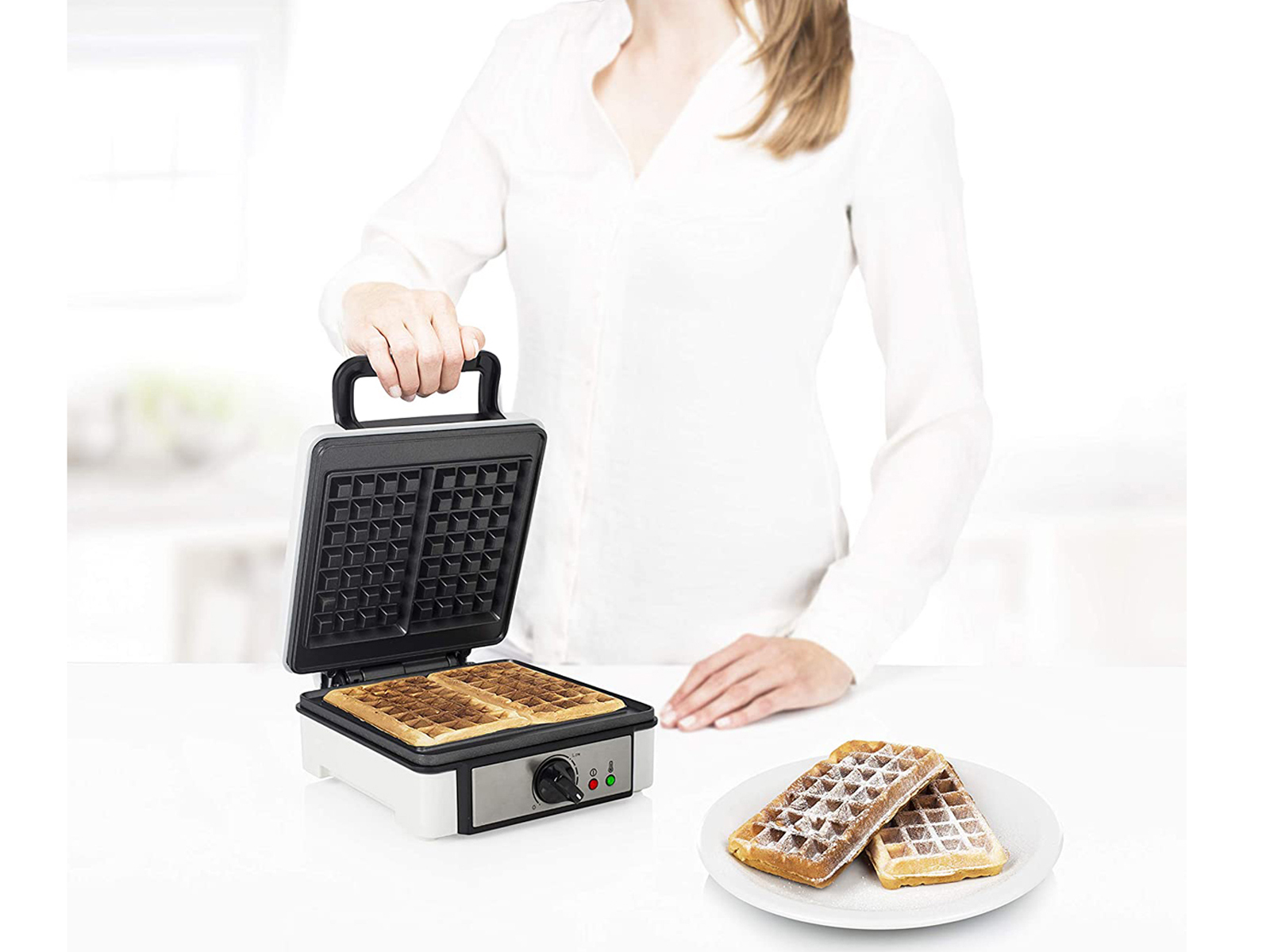 Frau benutzt Waffeleisen. Zwei Waffeln liegen auf einem Teller daneben.