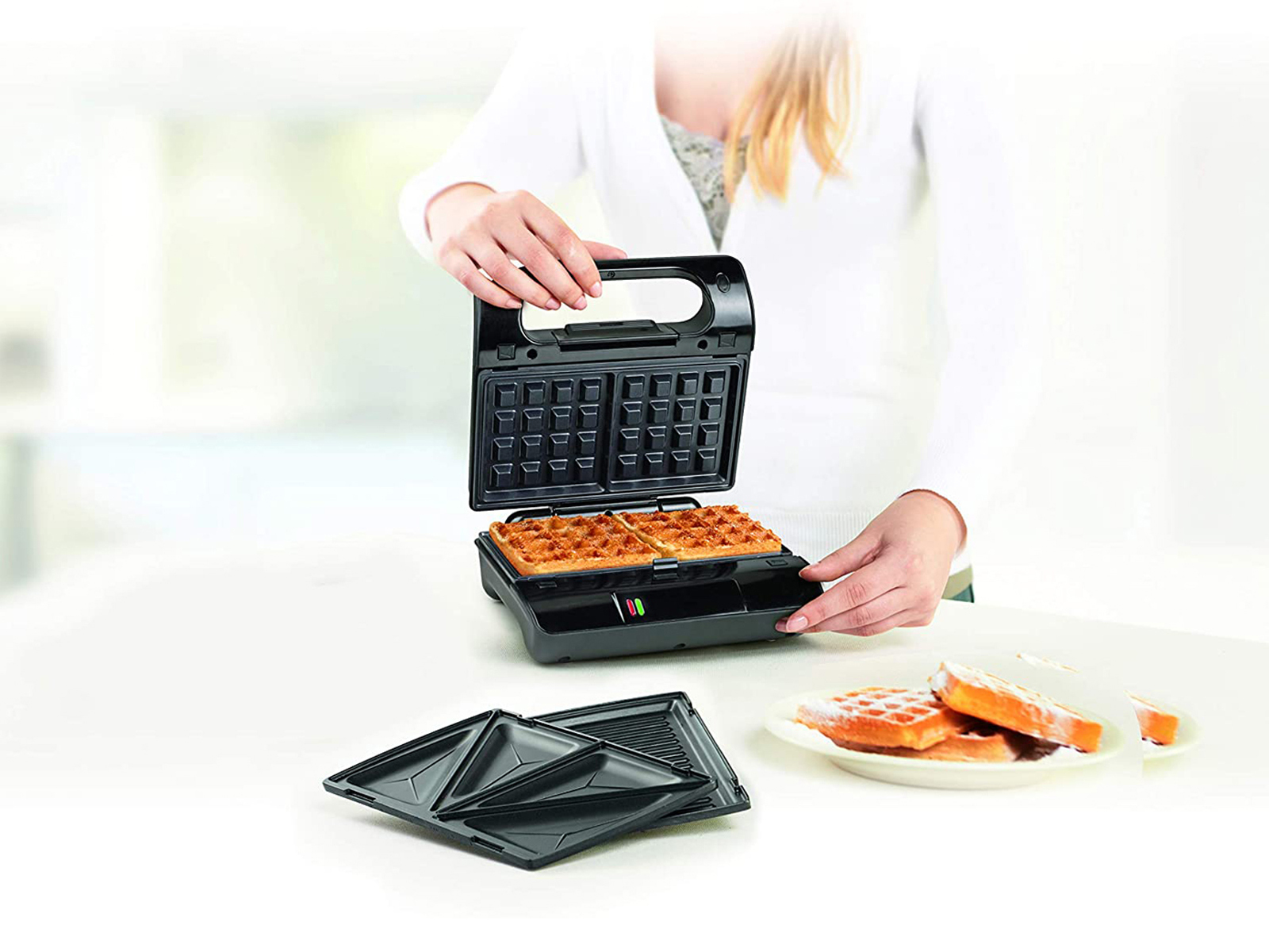 Person öffnet Waffeleisen mit zwei gebackenen Waffeln und separater Waffelform.