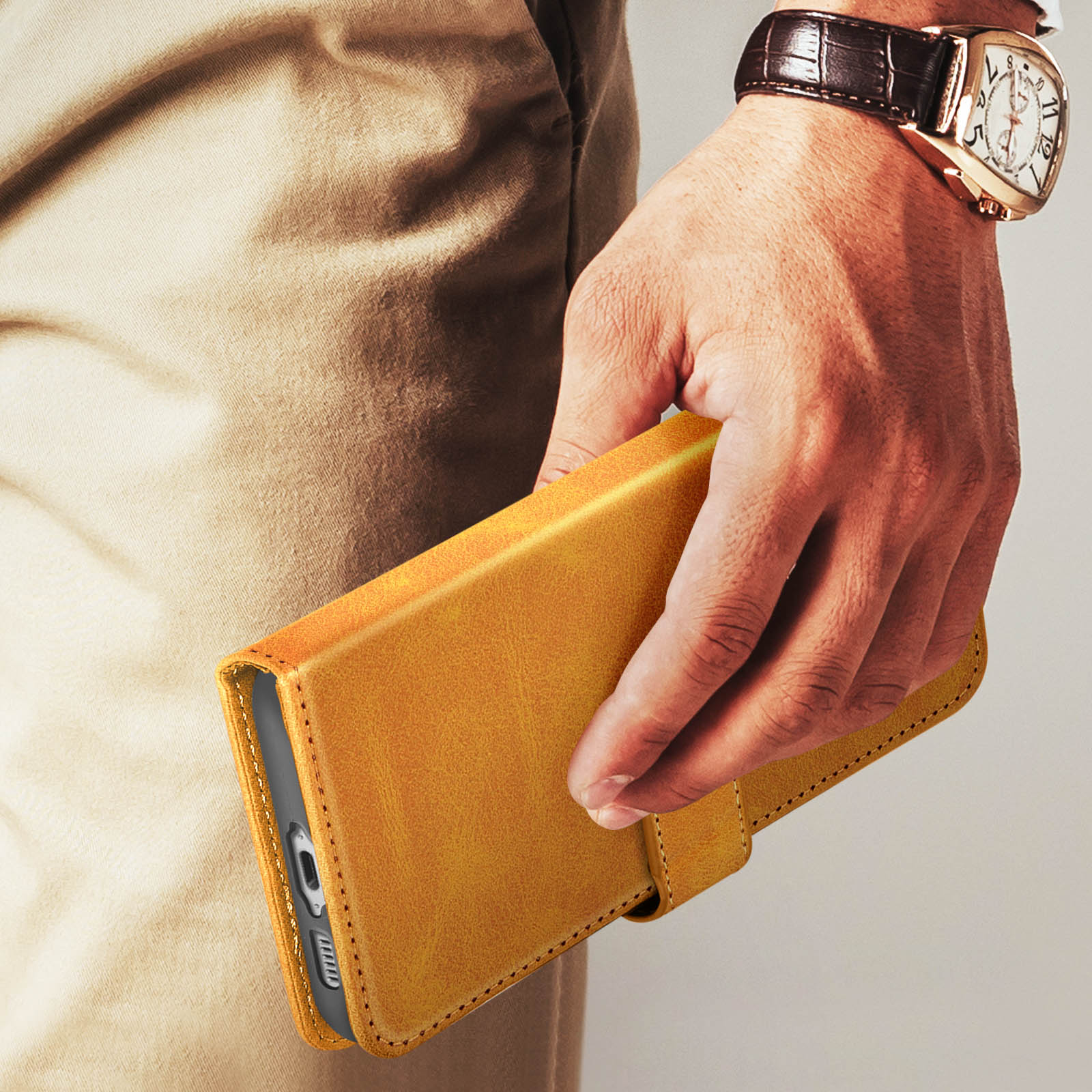 Una mano che tiene una custodia per telefono in pelle gialla, con un orologio al polso.