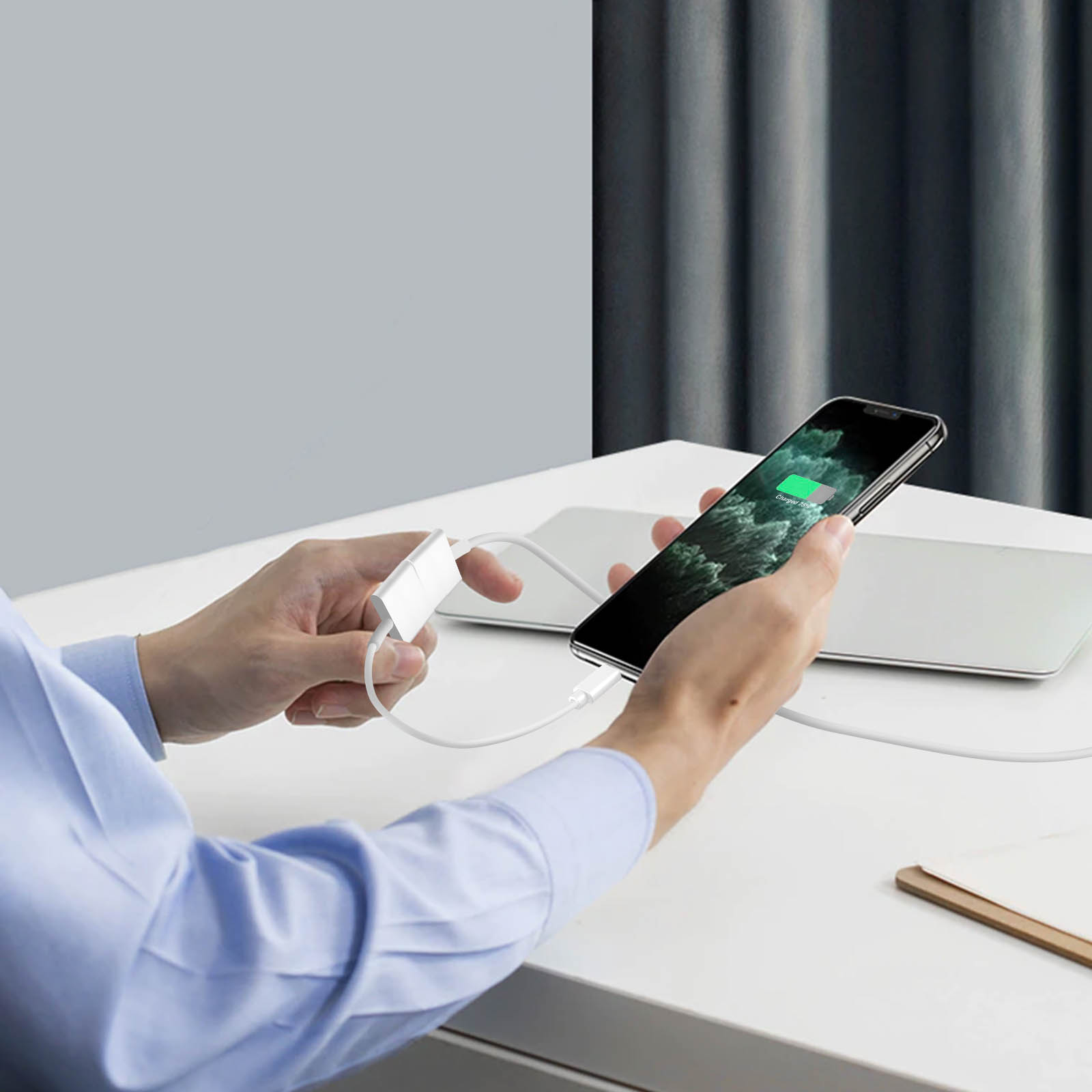 Hände einer Person, die ein Ladegerät halten, das mit einem Telefon und einem Laptop verbunden ist.