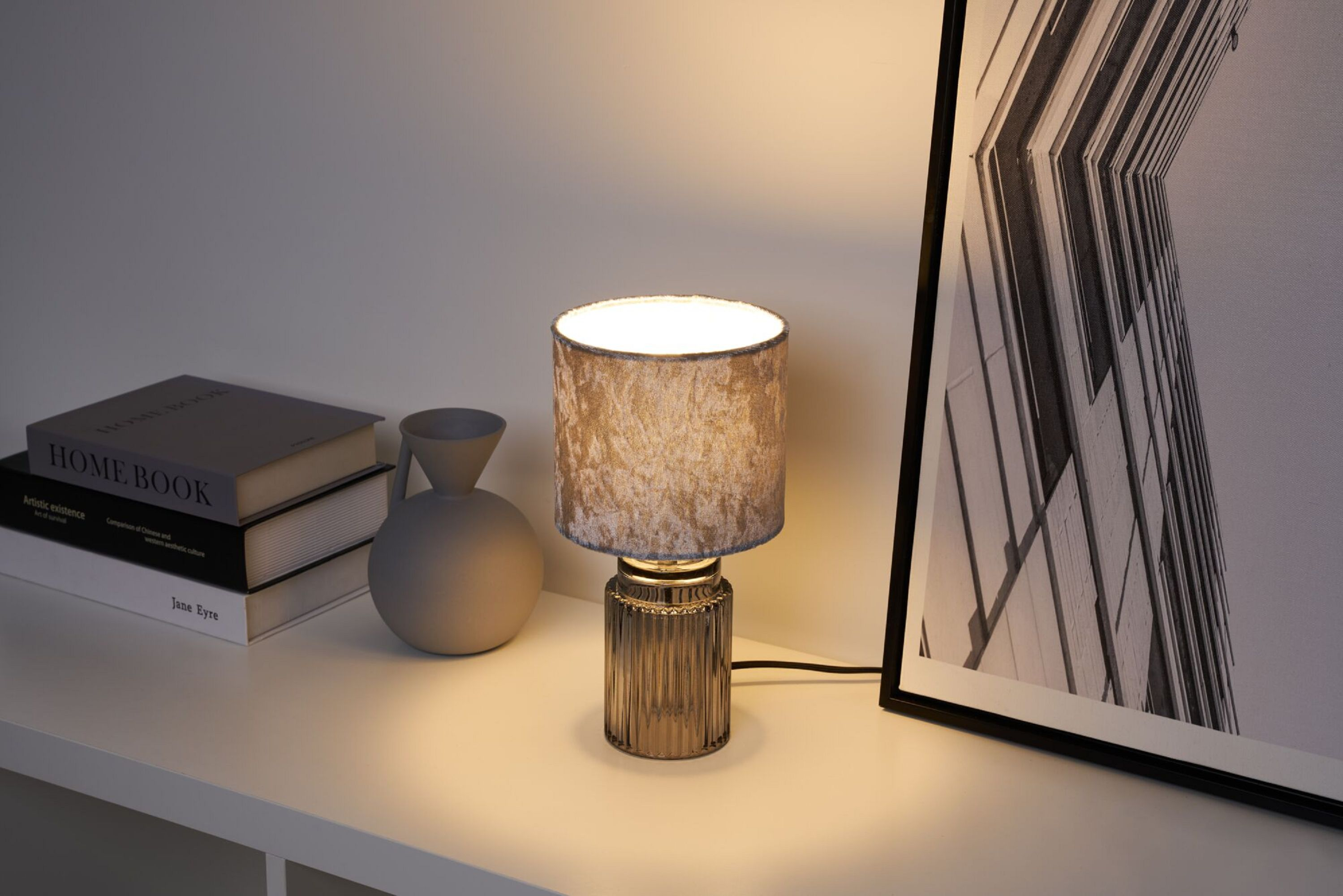 Eine Tischlampe mit strukturiertem Schirm und einer Vase sowie Büchern auf weißer Oberfläche.