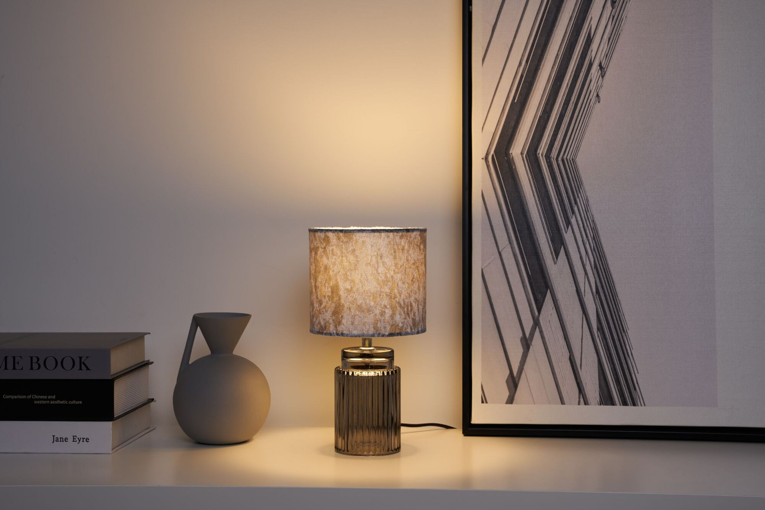 Eine Tischlampe mit strukturiertem Lampenschirm. Der Hintergrund zeigt Kunstwerke.
