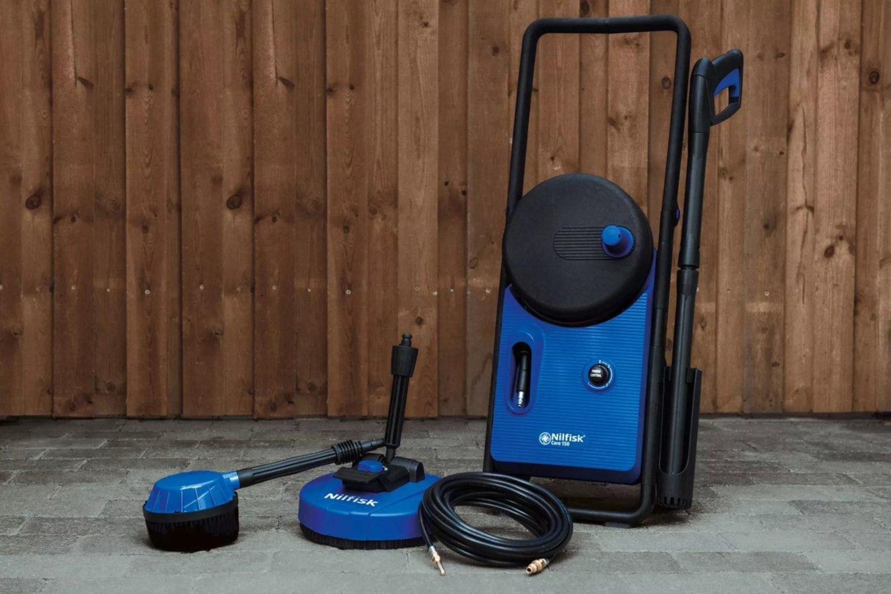 Niebiesko-czarna myjka ciśnieniowa z akcesoriami. Jest ustawiona na utwardzonej nawierzchni.