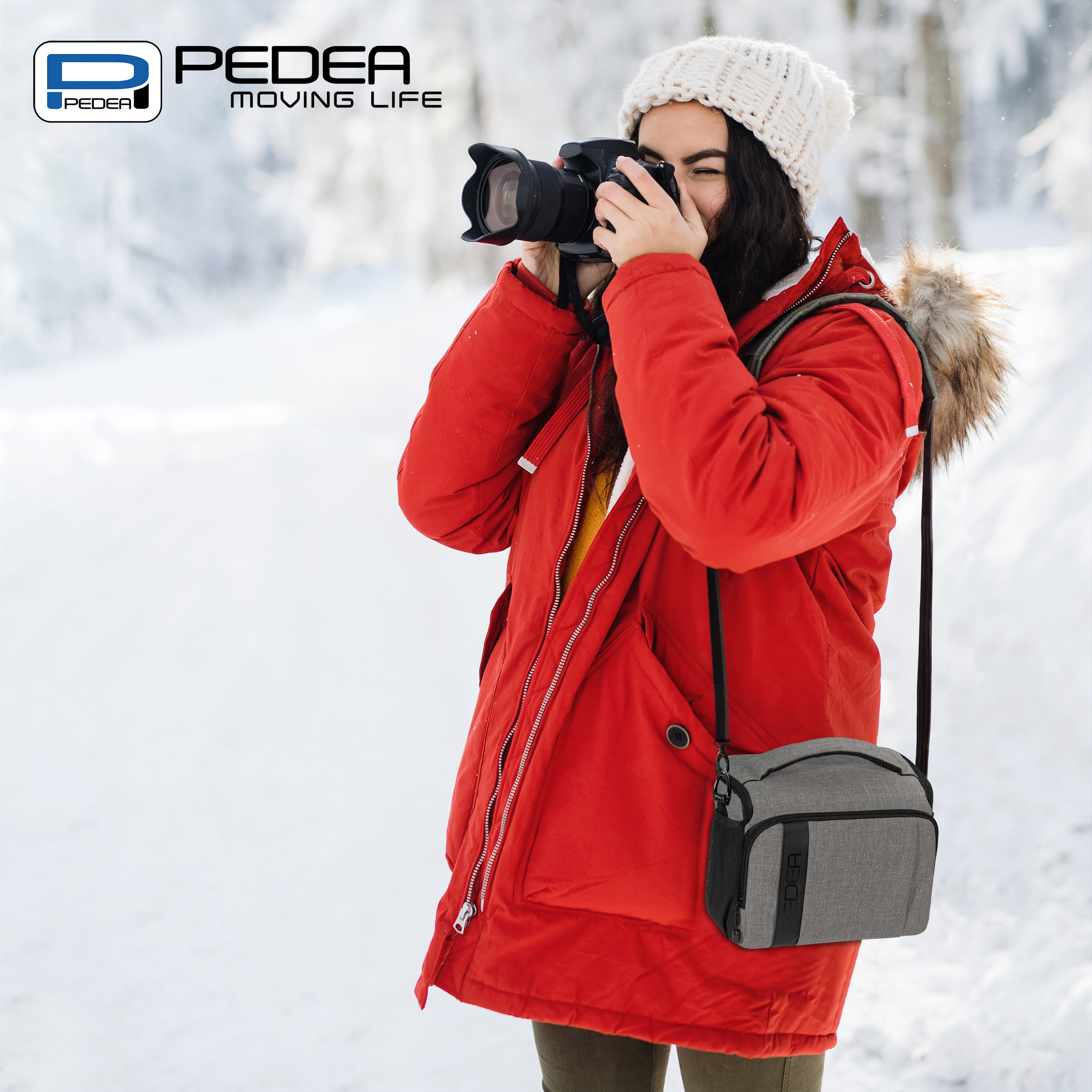 Eine Person macht ein Foto in einem verschneiten Wald mit einer Kamera und einer grauen Tasche.
