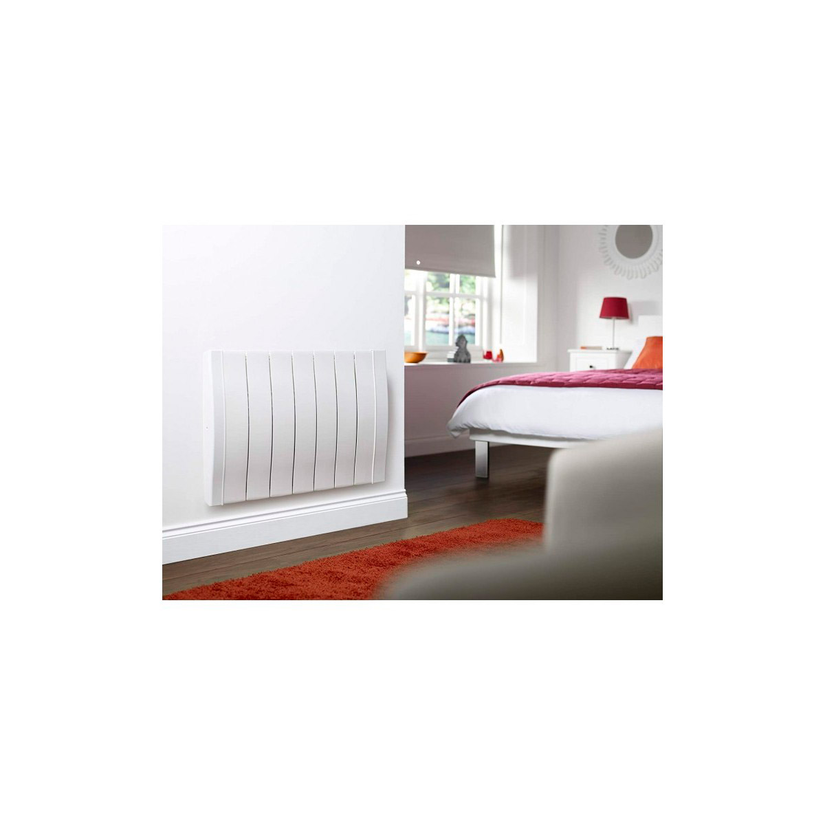 Radiador eléctrico blanco montado en la pared en una habitación con cama y alfombra roja.