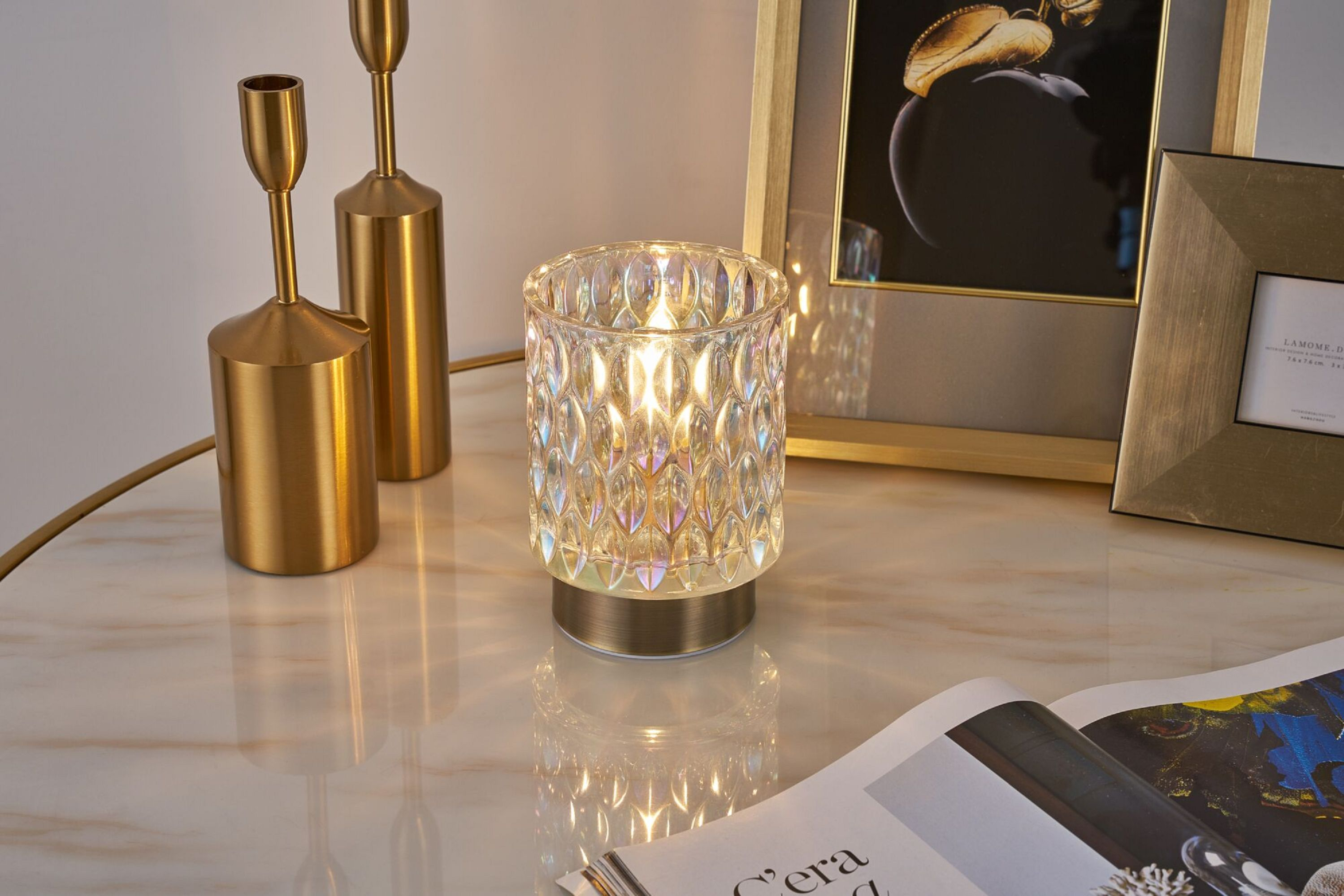 Lampa dekoracyjna z wzorzystym szklanym kloszem i złotą podstawą, na marmurowym stole.