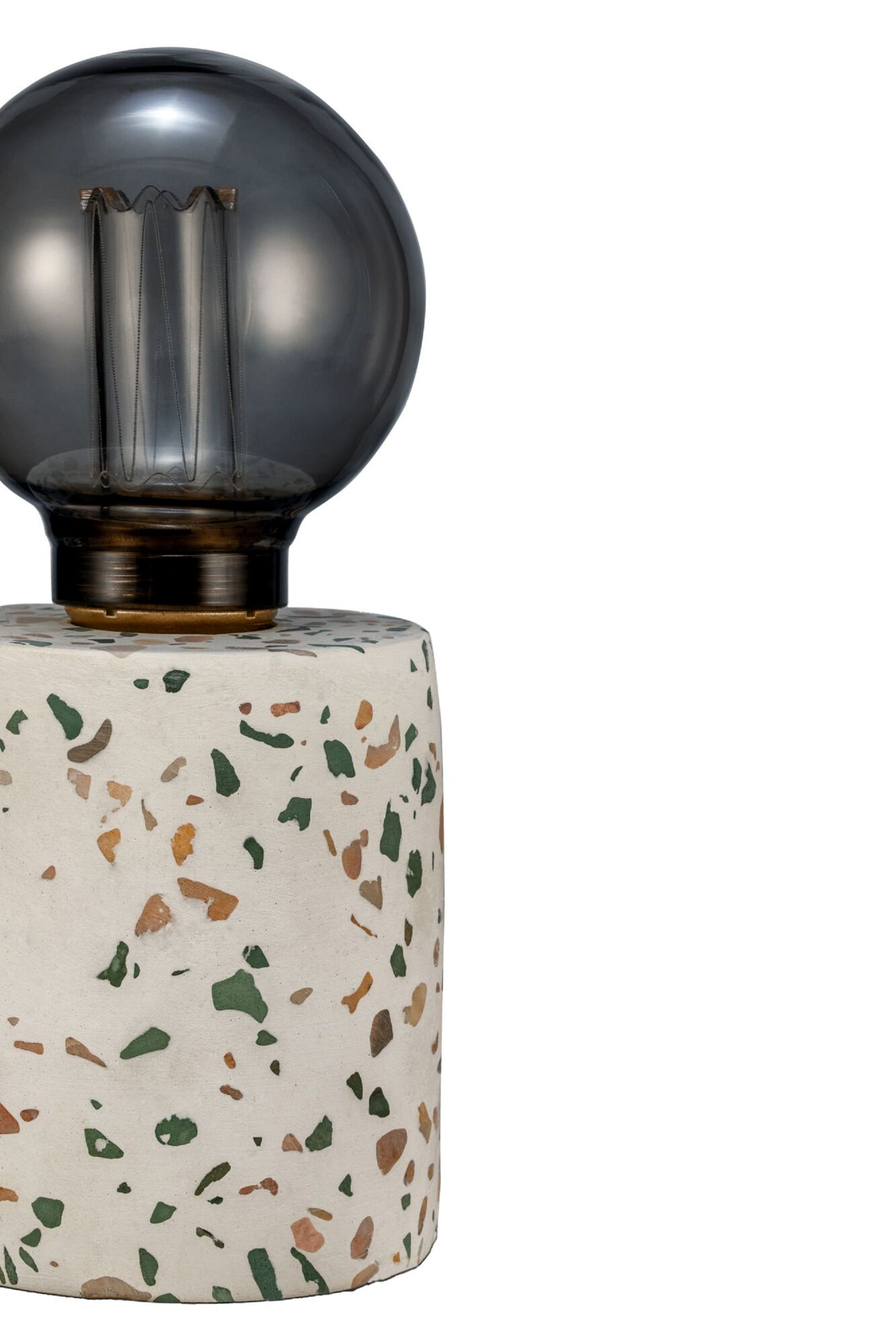 Lampa z podstawą z lastryko, szarą żarówką i białym tłem.